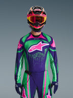 Set d'équipement Alpinestars Techstar Nomur 2026, pilote de motocross portant un maillot de course vert et violet vif avec des accents roses, ensemble assorti avec casque et lunettes multicolores, tenue de moto tout-terrain haute performance