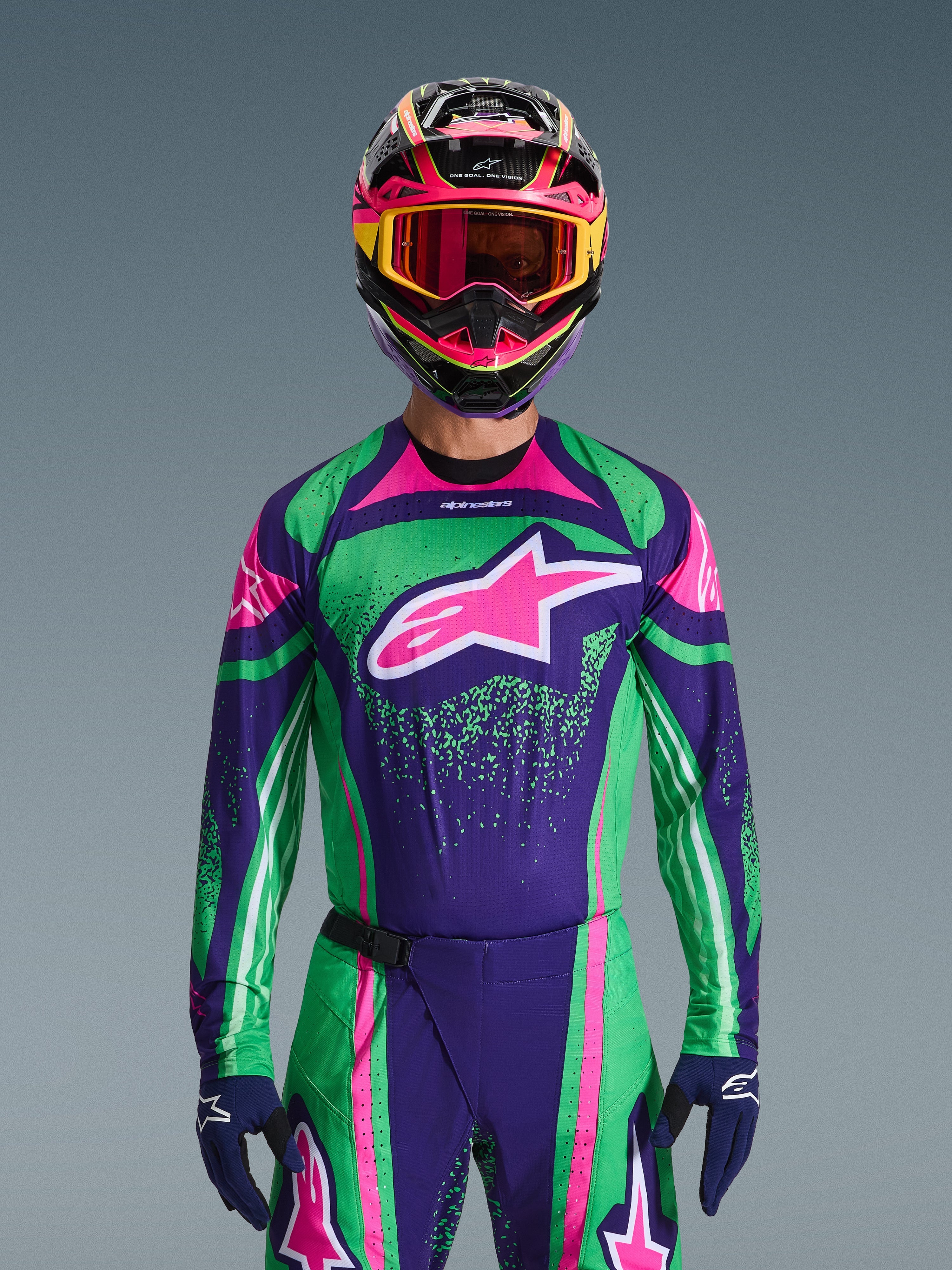 Set d'équipement Alpinestars Techstar Nomur 2026, pilote de motocross portant un maillot de course vert et violet vif avec des accents roses, ensemble assorti avec casque et lunettes multicolores, tenue de moto tout-terrain haute performance