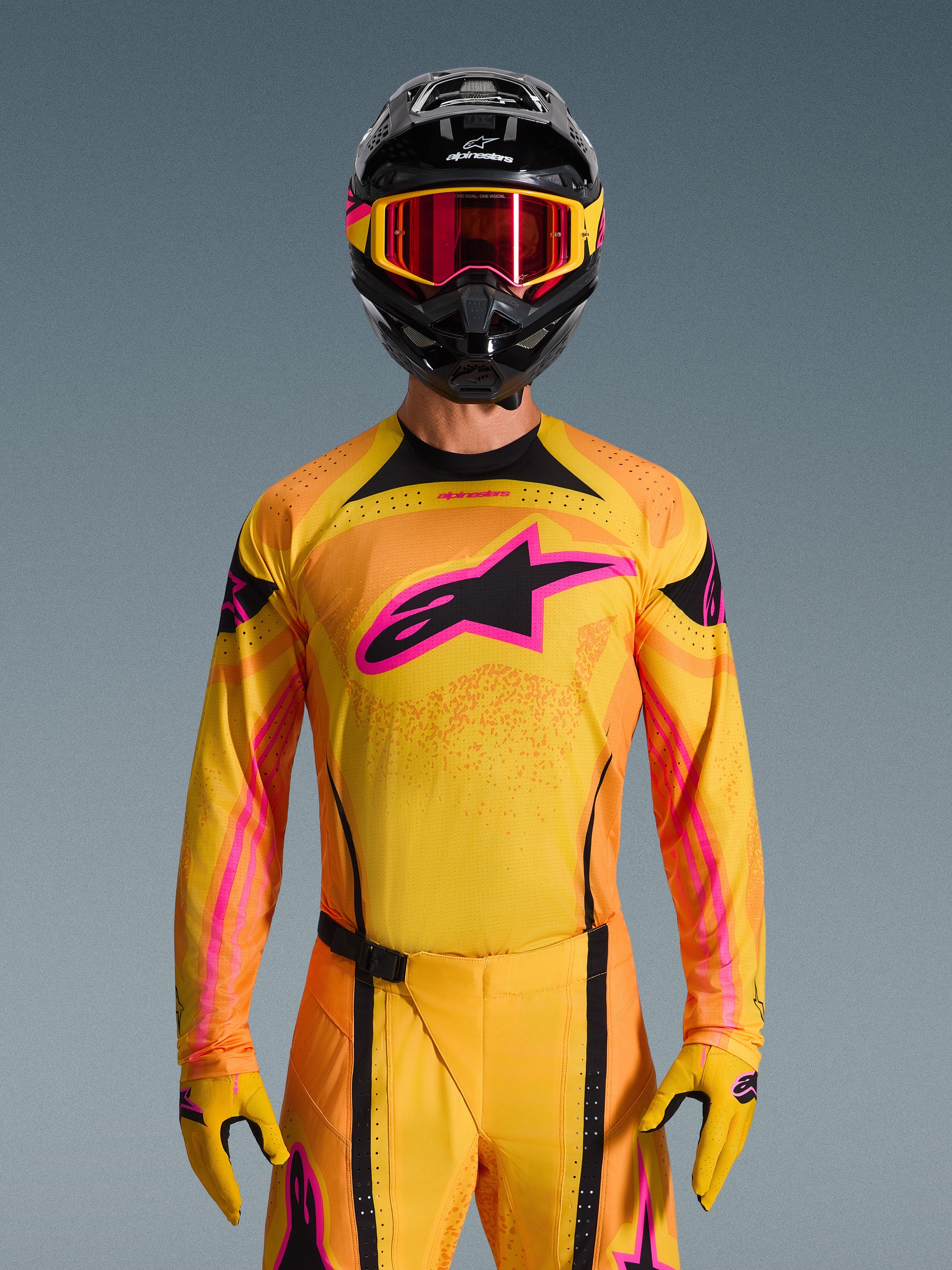 Alpinestars 2026 Techstar Nomur Gear Set, Motocross-Fahrer trägt gelbes und orangefarbenes Jersey und Hose mit leuchtend rosa Akzenten, schwarzer Helm mit gelben und rosa Grafiken, rot getönte Brille mit gelbem Rahmen, abgestimmtes Performance-Rennoutfit