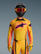 2026 Techstar Nomur Trikot in Orange, Gelb und Pink, getragen von einem Motocross-Fahrer mit einem passenden schwarzen Helm und pinkfarbener Brille, mit einem großen pinkfarbenen Alpinestars-Logo auf der Brust, athletische Rennpassform für Offroad-Performance.