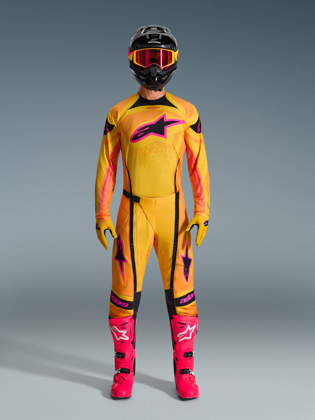 Motocross-Fahrer im 2026 Techstar Nomur Trikot in Orange, Gelb und Pink, kombiniert mit passender Motocross-Hose, schwarzem Helm mit pinker Brille und leuchtend pinken Stiefeln, athletische Race-Fit-Ausrüstung für Offroad-Wettkämpfe