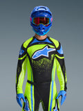Motocross rider wearing the Alpinestars 2026 Techstar Nomur Jersey in Dark Navy and Yellow Fluo with blue accents, featuring a large blue logo on the chest, matching blue helmet and goggles, coordinated racing gear for off-road competition