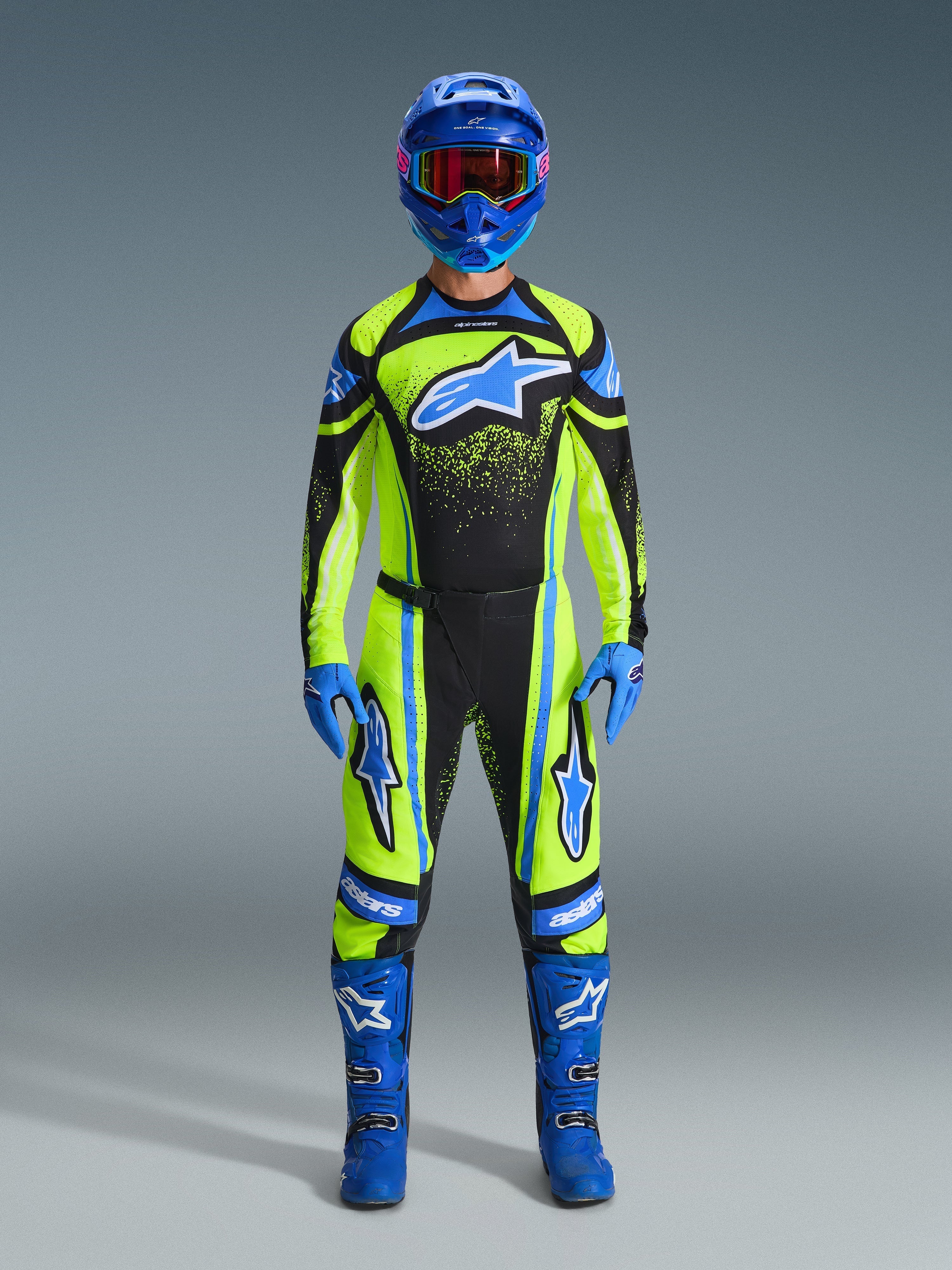 Motocross rider wearing complete racing gear, 2026 Techstar Nomur Jersey in yellow fluo and dark navy, matching motocross pants, blue helmet with red-tinted goggles, blue gloves, and blue boots, coordinated professional outfit for off-road racing
