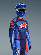 Ensemble d'équipement Alpinestars Techstar Nomur 2026, maillot et pantalon de motocross bleu marine foncé, orange et bleu UCLA, porté par un pilote avec casque et gants bleus assortis, présentant des graphismes de logo audacieux et une coupe athlétique de course.