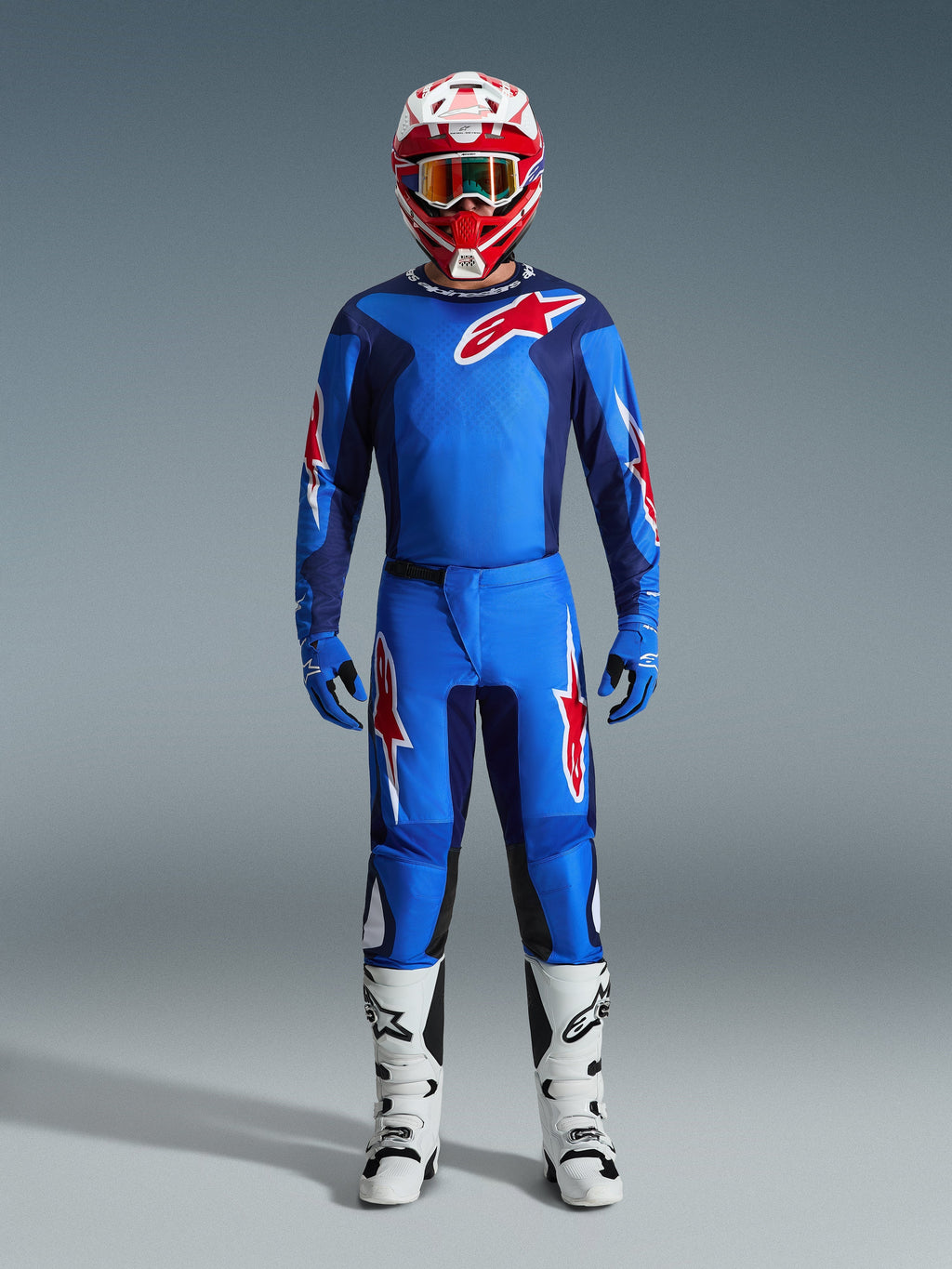 Motocross rider wearing the Alpinestars 2026 Fluid Grid Jersey in Blue and Red, matching blue pants with white and red star logos, red and white helmet with mirrored goggles, blue gloves, and white and black racing boots, complete off-road gear set.
