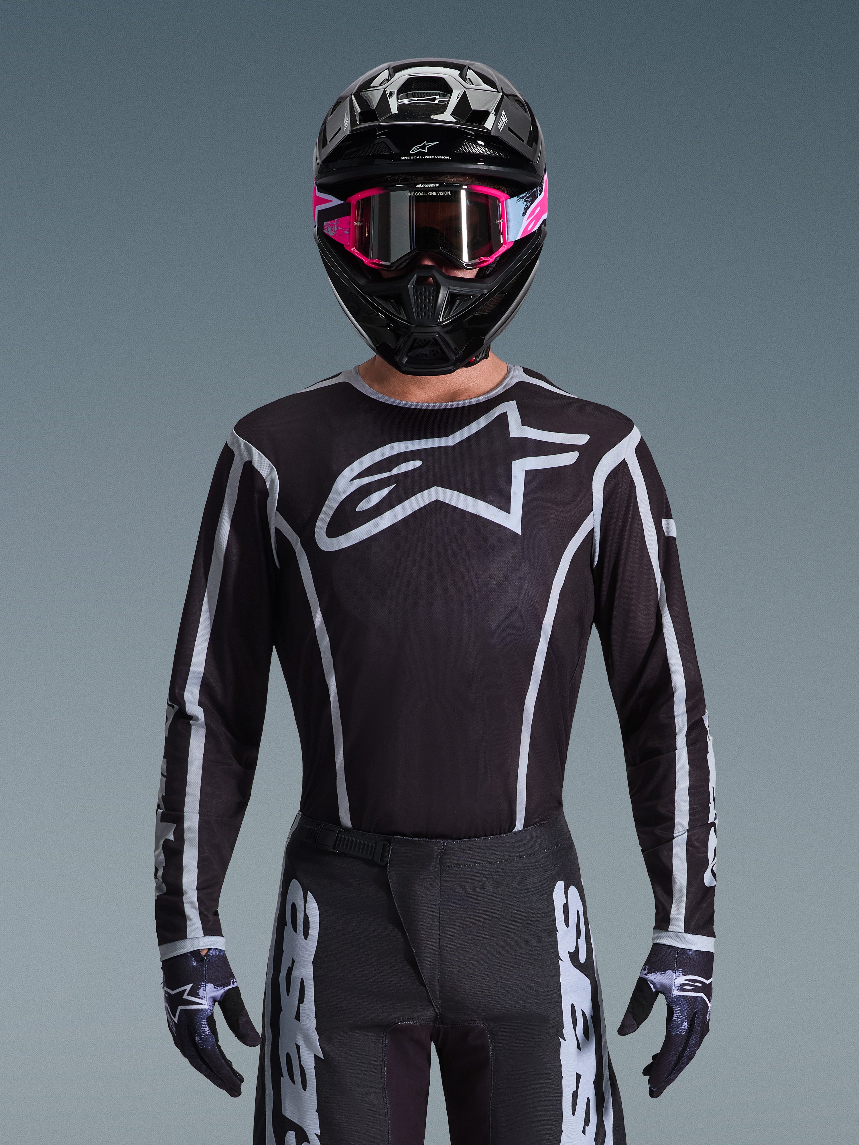 Ensemble d'équipement Alpinestars Fluid Apex 2026, maillot et pantalon de motocross noir et blanc, avec un grand logo sur la poitrine et des lignes géométriques, porté avec un casque noir et des lunettes roses, équipement de performance pour le motocross tout-terrain
