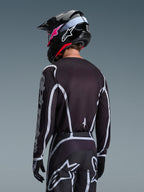 Motocross rider from the back wearing the Alpinestars 2026 Fluid Apex Jersey in Black and Gray, matching motocross pants with white accents, black helmet with pink branding, coordinated outfit for off-road racing