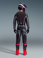 Pilote de motocross vu de dos portant l'ensemble d'équipement Alpinestars 2026 Fluid Apex, maillot et pantalon noirs avec lignes géométriques grises et logos étoilés, casque noir avec accents roses, bottes rouge vif et noires, tenue de motocross coordonnée