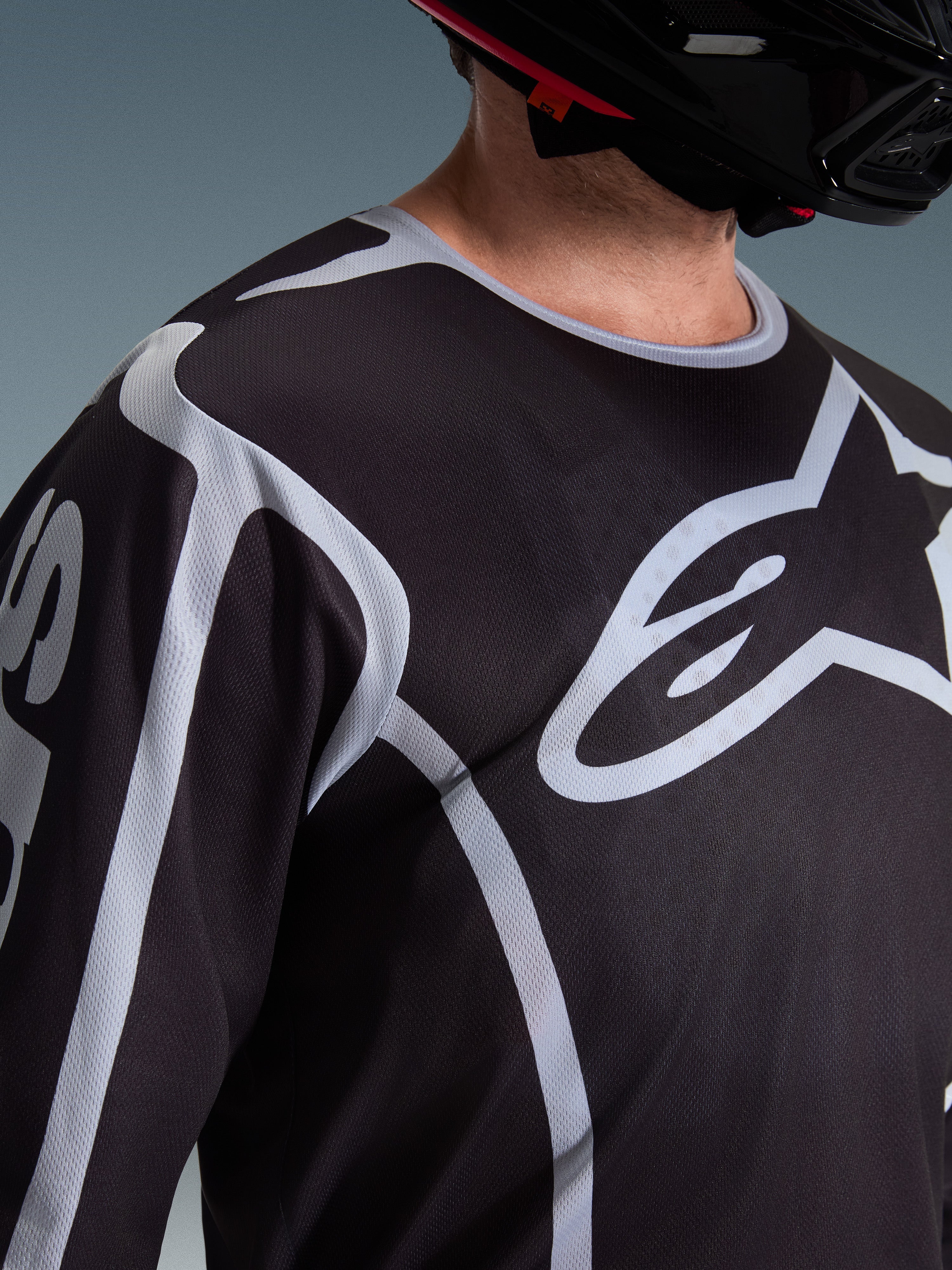 Maillot Alpinestars Fluid Apex 2026, maillot de motocross, noir et gris, avec un grand logo Alpinestars sur la poitrine, col sport, porté avec un casque noir, équipement de performance pour la conduite tout-terrain