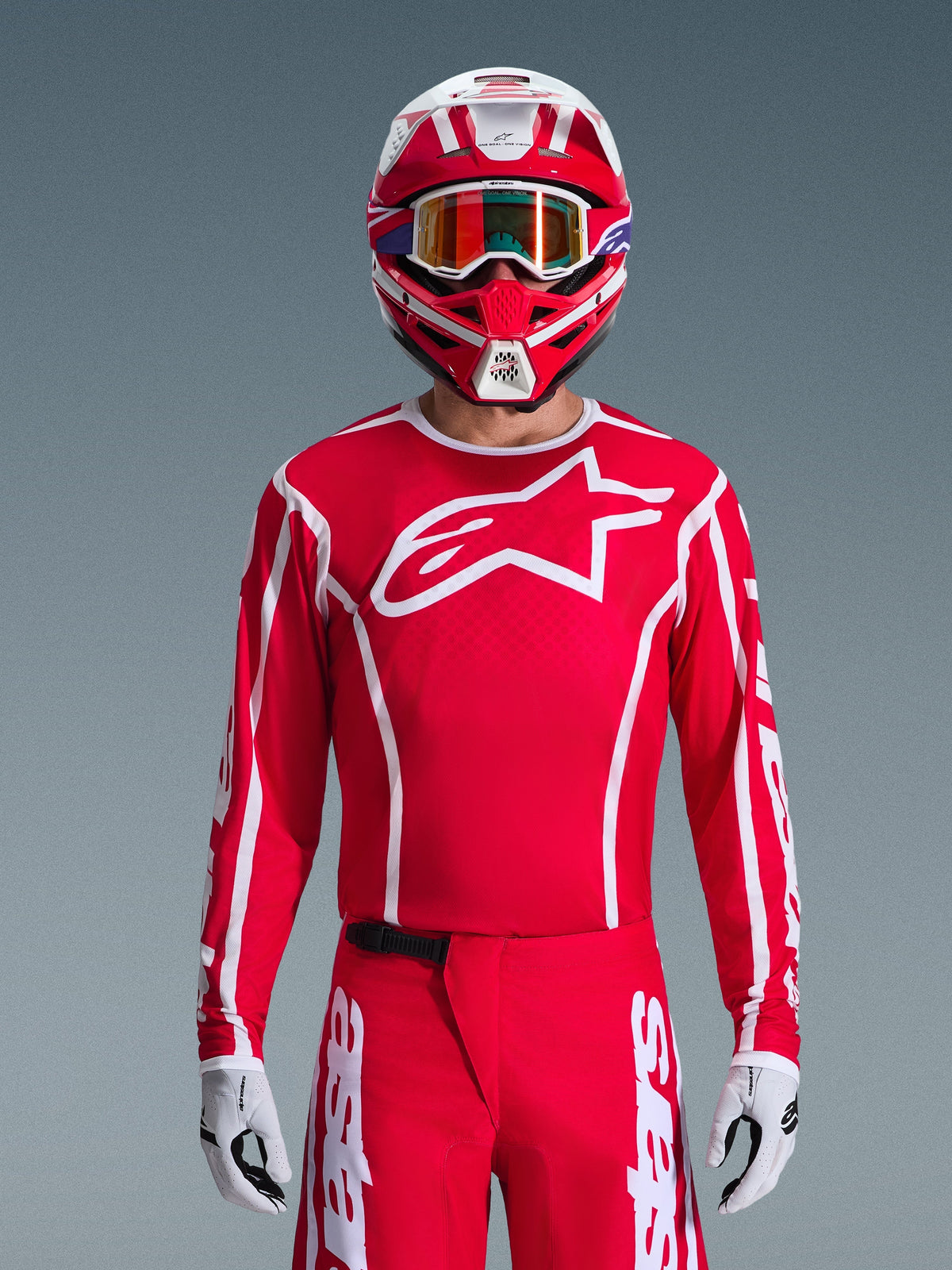 Maillot Alpinestars Fluid Apex 2026, maillot de motocross, rouge et blanc, porté par un pilote avec un casque rouge et blanc assorti et des lunettes orange, arborant un logo blanc proéminent sur la poitrine, coupe athlétique, faisant partie d'un ensemble d'équipement de course tout-terrain coordonné