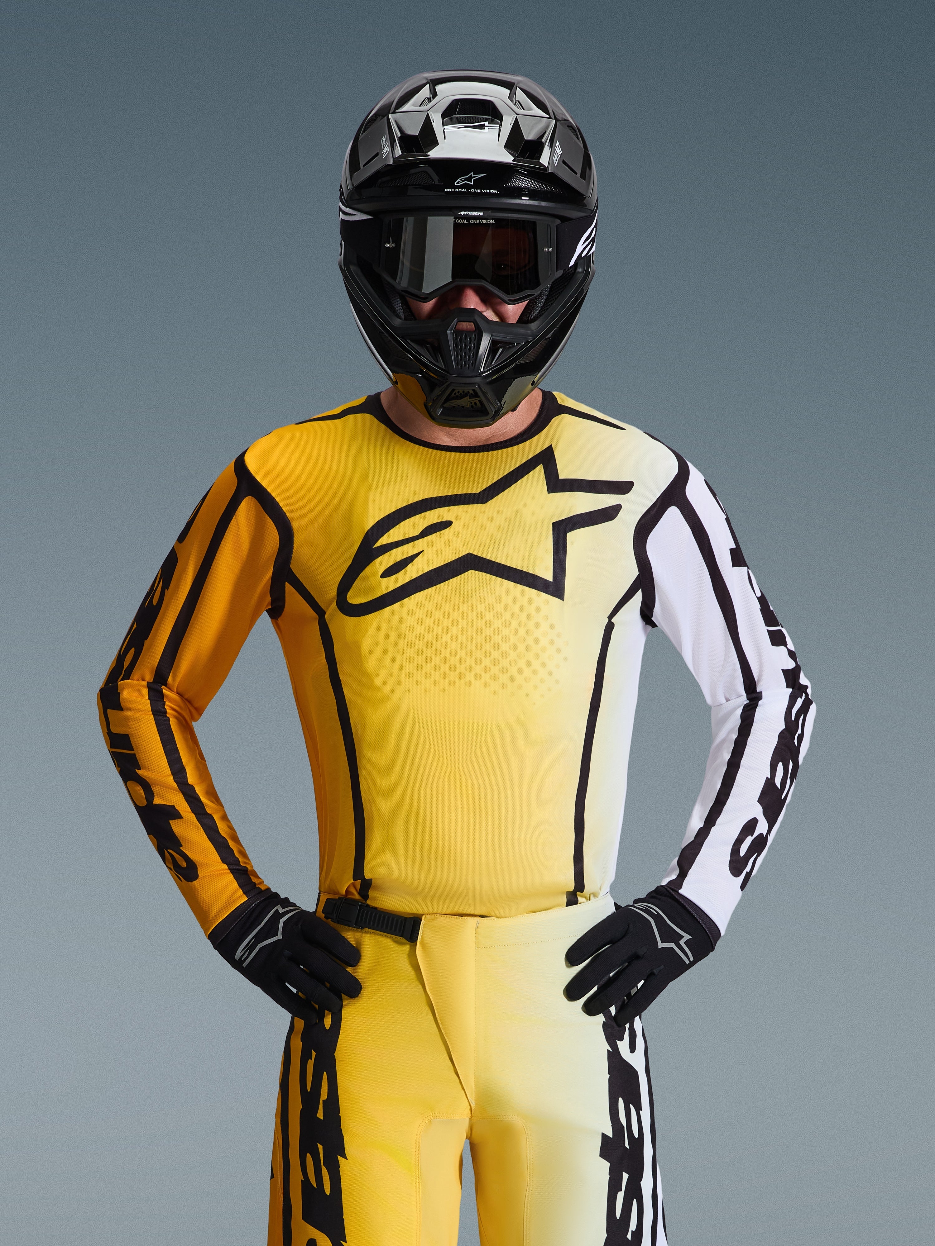 Maillot Alpinestars Fluid Apex 2026, maillot de motocross, jaune et noir avec une manche blanche et un grand logo noir sur la poitrine, porté dans le cadre d'une tenue de course complète avec pantalon assorti, casque noir et gants