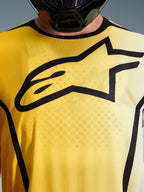 Alpinestars 2026 Fluid Apex Jersey, motocross jersey, felgeel en zwart, close-up met een groot zwart Astar-logo op de borst, ademend vochtafvoerend polyfabric met een sportkraag