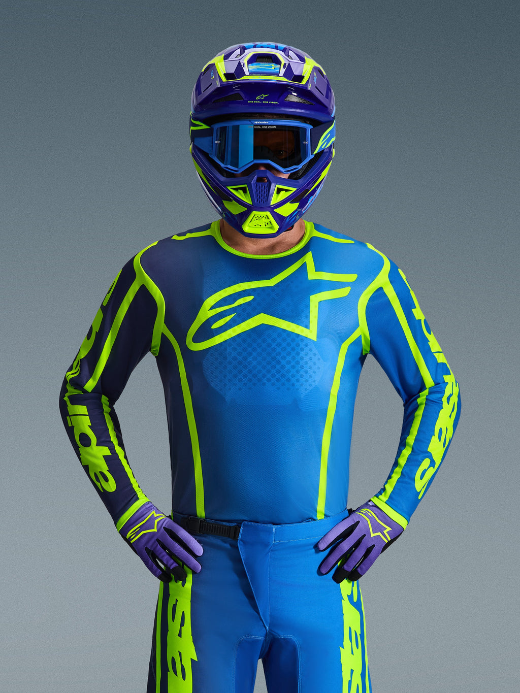 Alpinestars 2026 Fluid Apex Gear Set, Motocross-Fahrer in kompletter Schutzausrüstung, petrolblaues Jersey mit neongelben Akzenten und einem dunkelvioletten Ärmel, dazu passende petrolblaue Hose und lila Handschuhe, farblich abgestimmter lila-neongelber Helm mit blauer Brille, Frontansicht für eine Offroad-Rennsport-Ästhetik