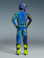 Alpinestars 2026 Fluid Apex Ausrüstungsset, Rückansicht eines Motocross-Fahrers in einem blau-dunkelblauen Jersey und passender Hose mit leuchtenden neongrünen Akzenten, neongelbe Stiefel und ein lila Helm, professionelles Offroad-Rennoutfit.