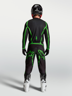 Alpinestars Fluid Apex V2 jersey, motocross jersey voor off-road rijden, zwart en fluogroen, achteraanzicht op model met witte motorlaarzen.