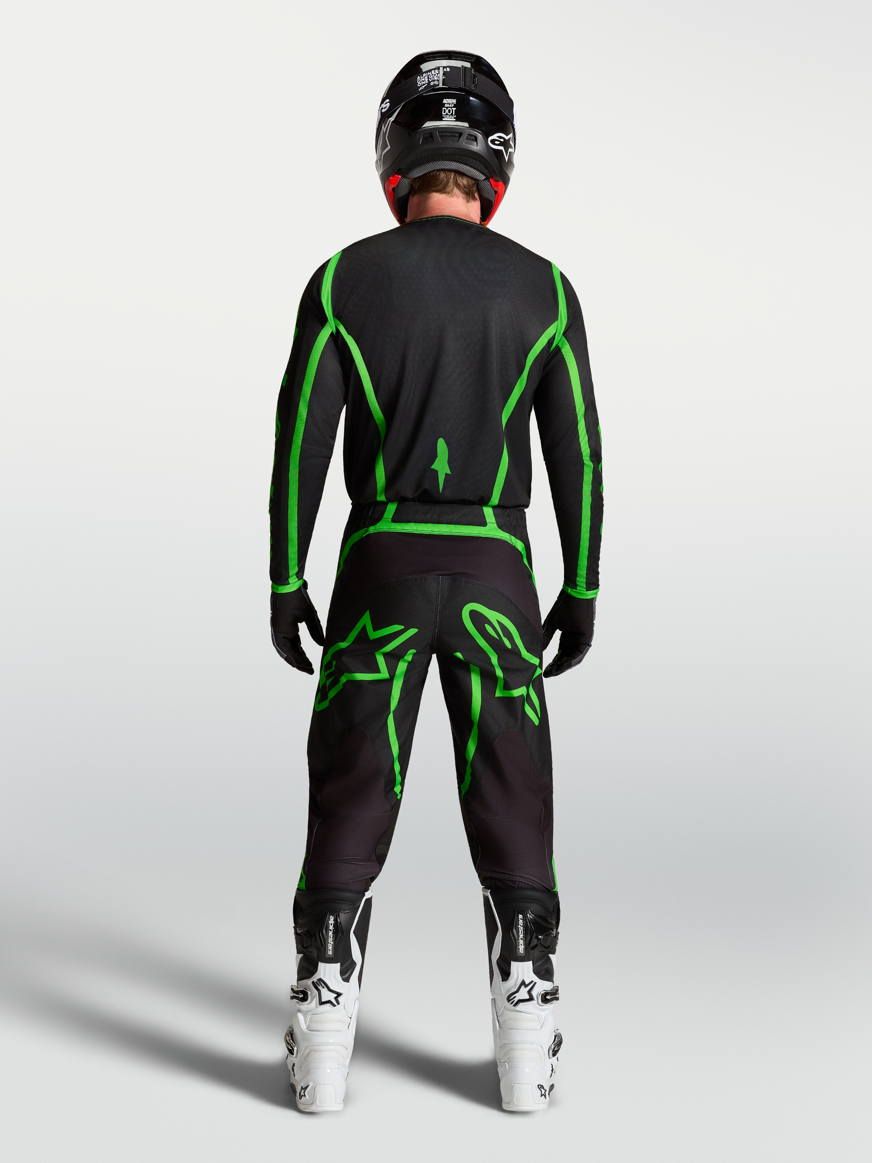 Alpinestars Fluid Apex V2 jersey, motocross jersey voor off-road rijden, zwart en fluogroen, achteraanzicht op model met witte motorlaarzen.