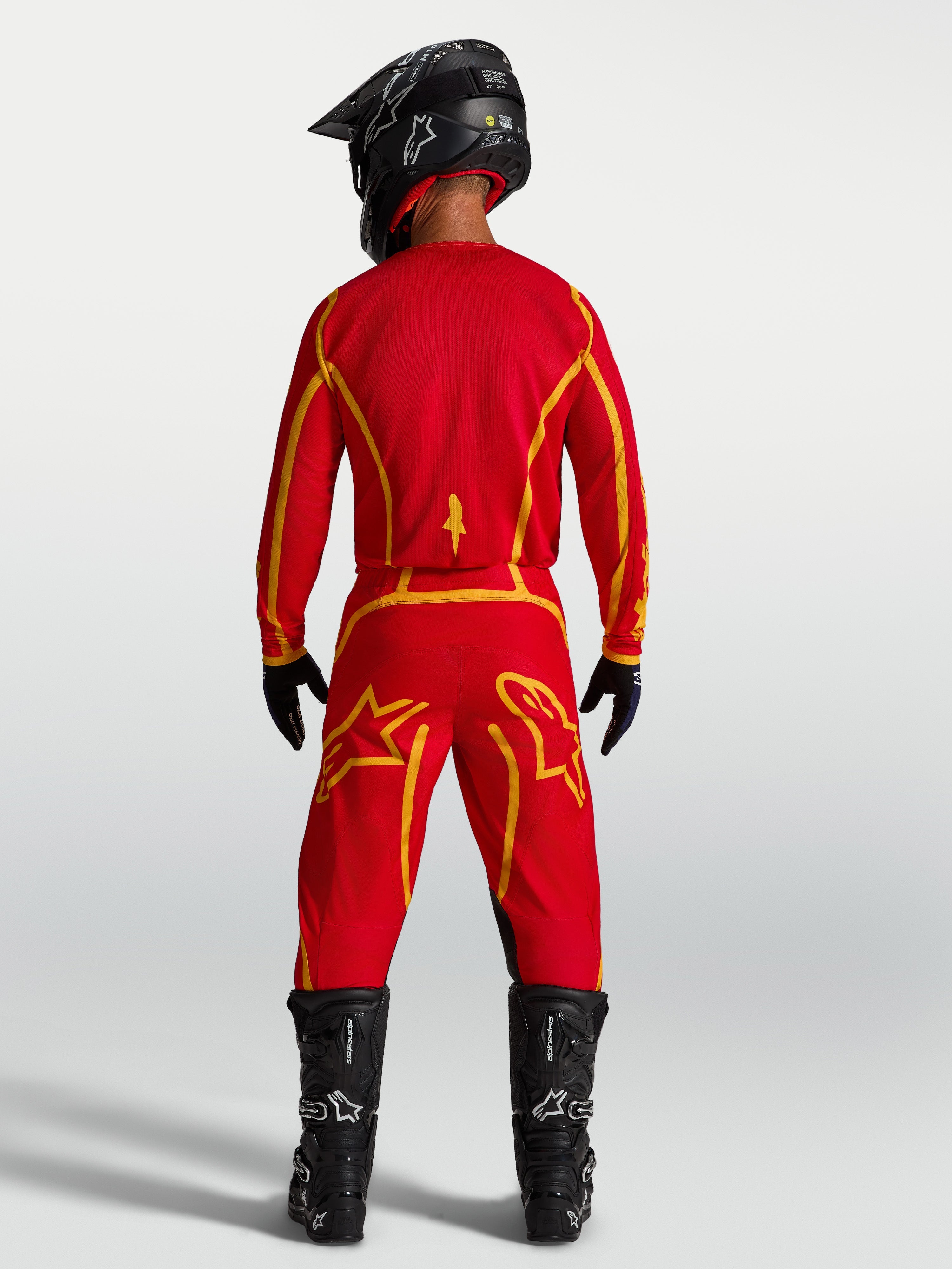 Alpinestars Fluid Apex V2 jersey, heren-motocrossjersey, rood en goud, achteraanzicht met motorlaarzen, vochtafvoerende stof.