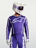 Alpinestars Maillot Fluid Apex V2, maillot de motocross pour homme, bleu et blanc, porté avec casque et gants, conçu pour le tout-terrain et la performance.