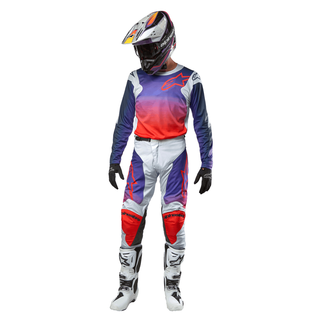 Motocross-Fahrer in kompletter Rennausrüstung, Alpinestars 2024 Racer Hoen Trikot mit lila bis hot-orangem Farbverlauf und hellgrauen Schultern, passende hellgraue Hose mit roten und lila Akzenten, abgestimmter Helm und weiße Stiefel, komplette Offroad-Rennausrüstung