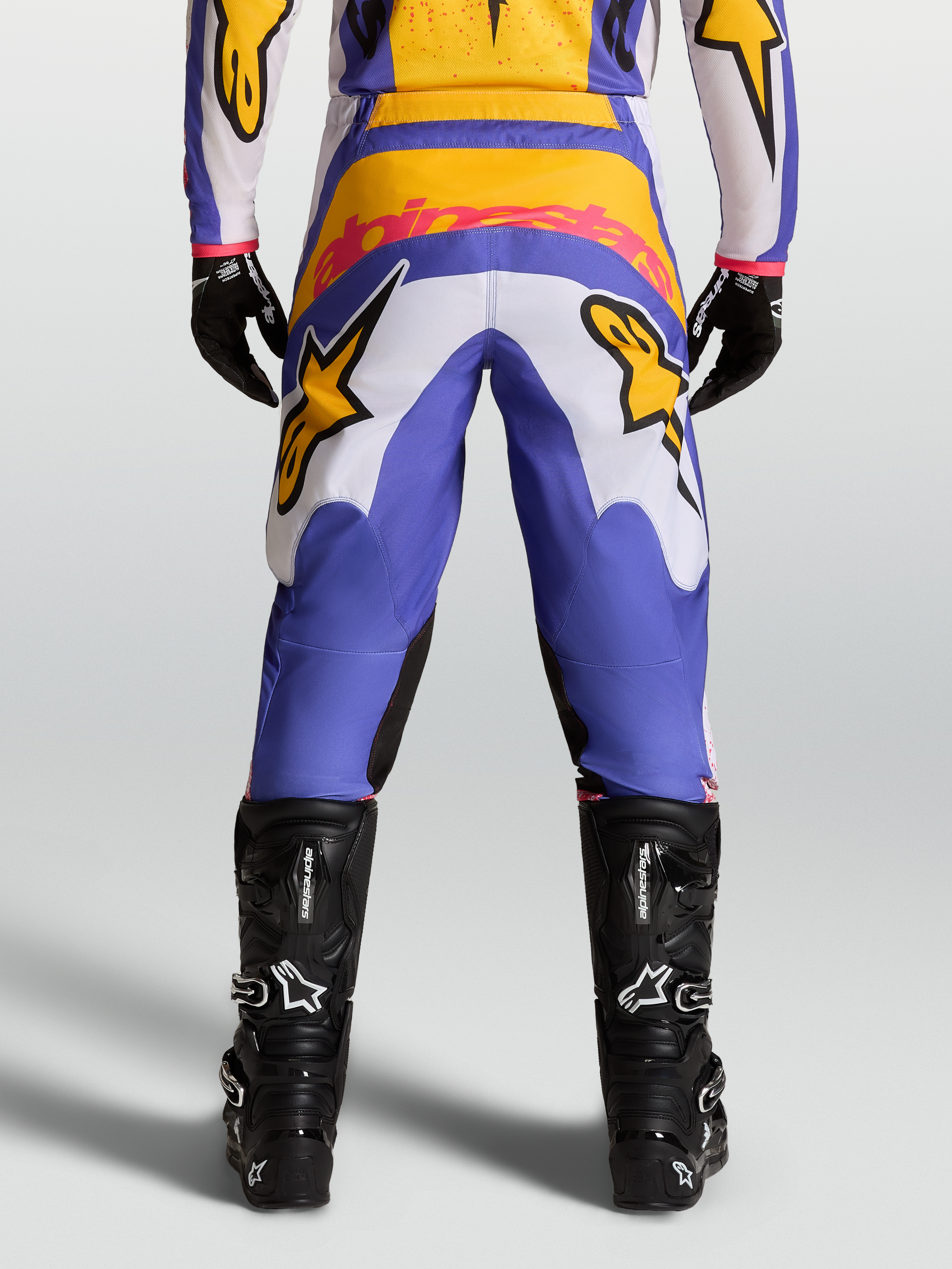 Alpinestars Fluid Drag broek, motorcrossbroek voor heren, blauw en goud, met stretch corduroy en zwarte motorlaarzen.