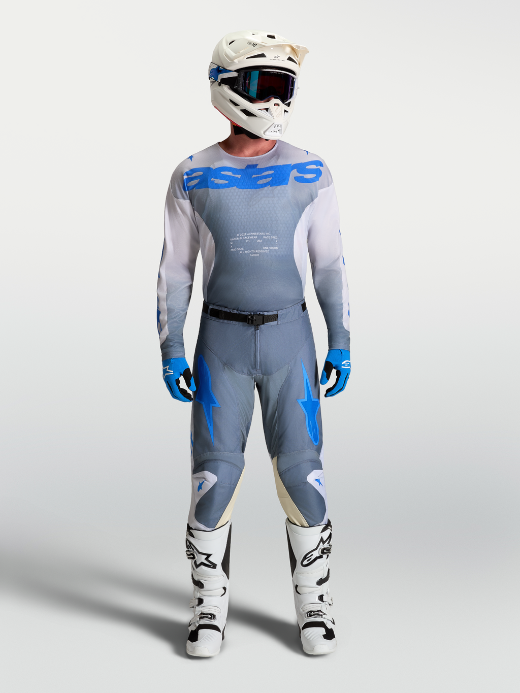 Alpinestars Racer Amber broek en jersey, heren motocrossuitrusting in grijs en UCLA blauw, met witte laarzen en helm, duurzame off-road race-uitrusting.