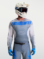 Alpinestars Racer Amber Trikot, Motocross-Ausrüstung für Herren, Grau und UCLA Blau, mit weißem MX-Helm und Schutzbrille.