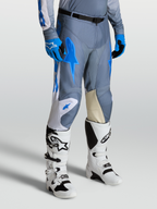 Alpinestars Racer Amber Broek voor heren, motocrossbroek in grijs en blauw, met goit lederen kniepanelen en witte Techstar laarzen.