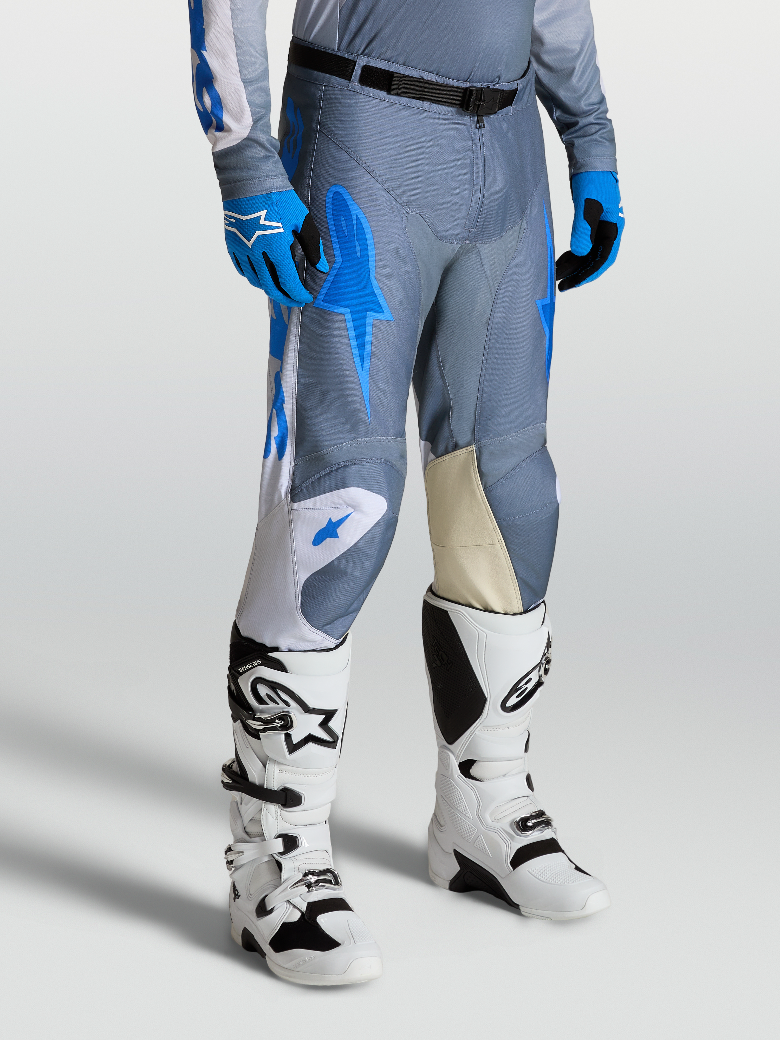 Alpinestars Racer Amber Broek voor heren, motocrossbroek in grijs en blauw, met goit lederen kniepanelen en witte Techstar laarzen.