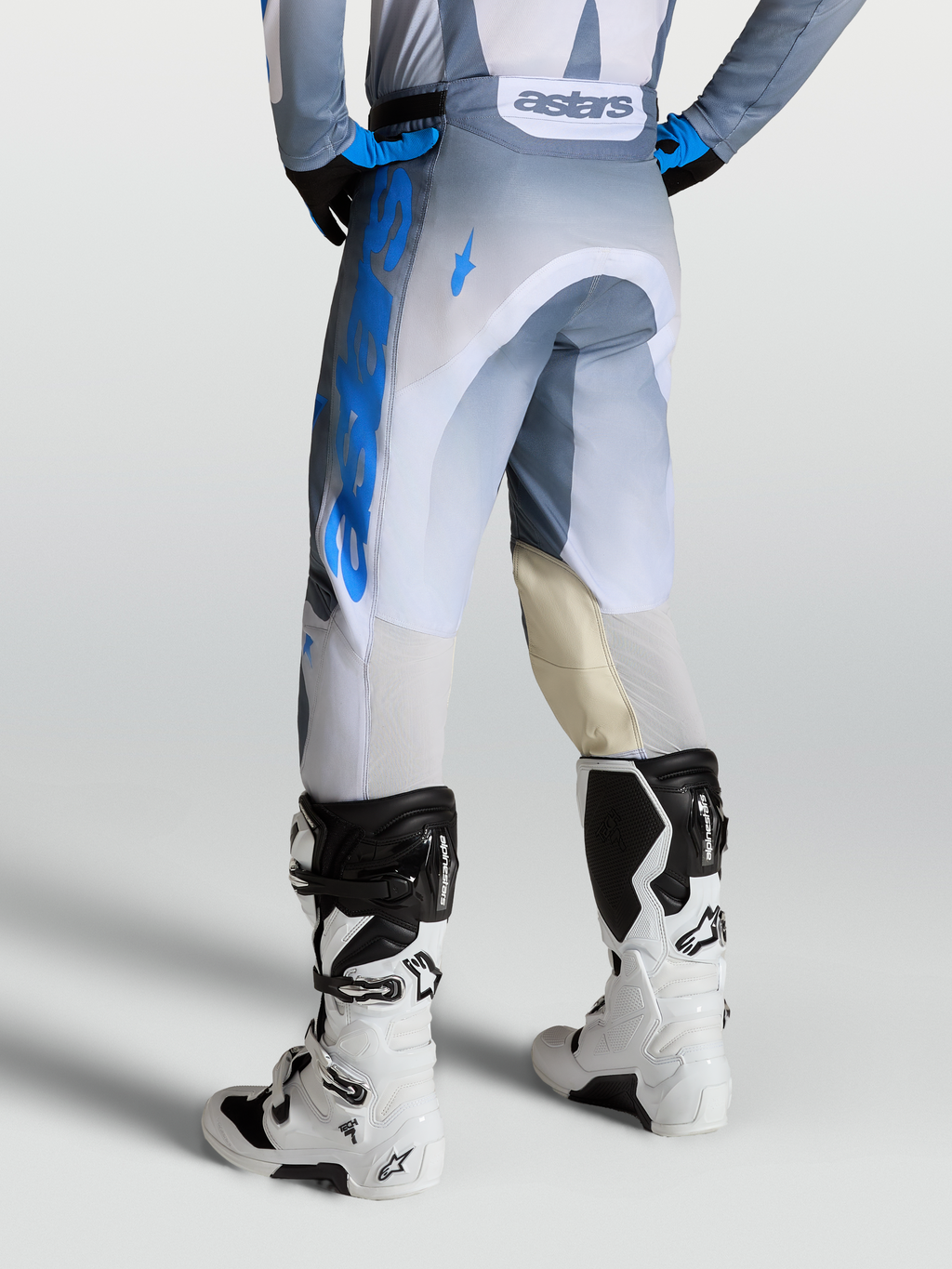 Alpinestars Racer Amber Broek, heren motocrossbroek in grijs en blauw, met lederen kniepanelen en witte motorlaarzen.