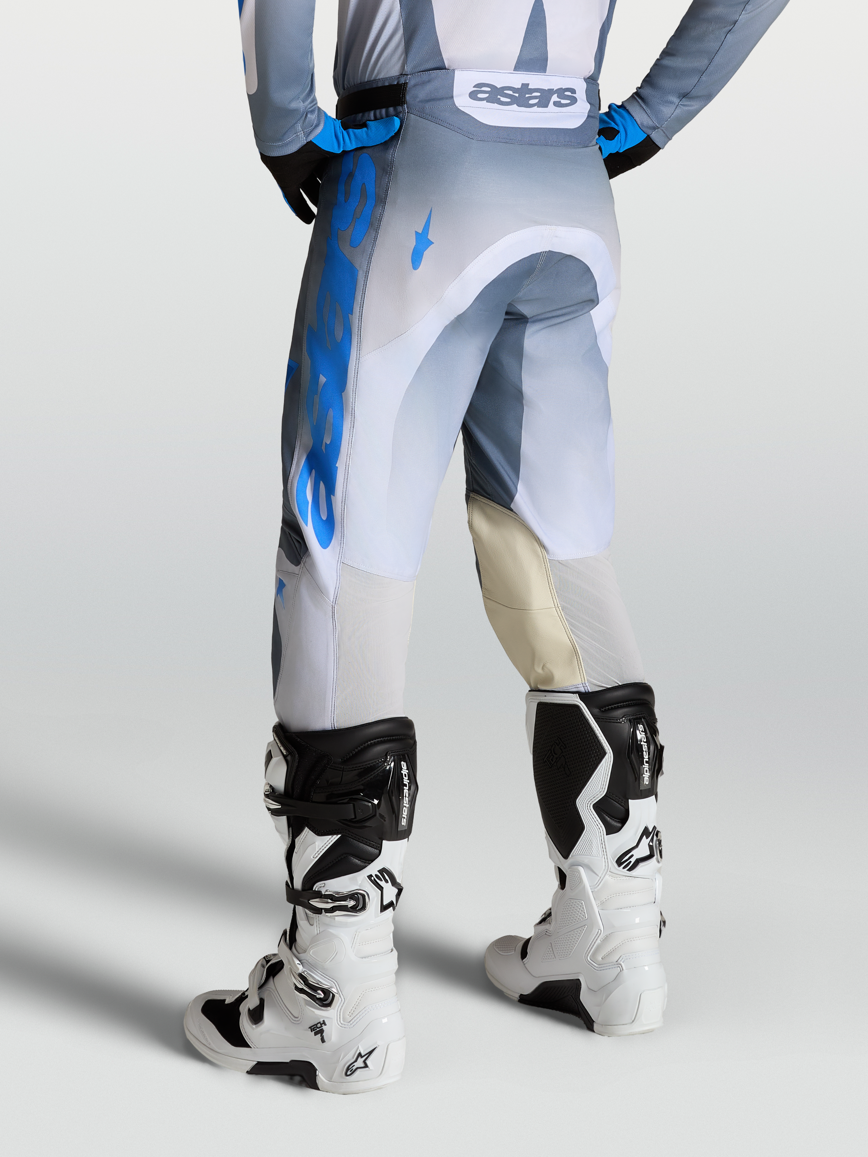Alpinestars Racer Amber Broek, heren motocrossbroek in grijs en blauw, met lederen kniepanelen en witte motorlaarzen.