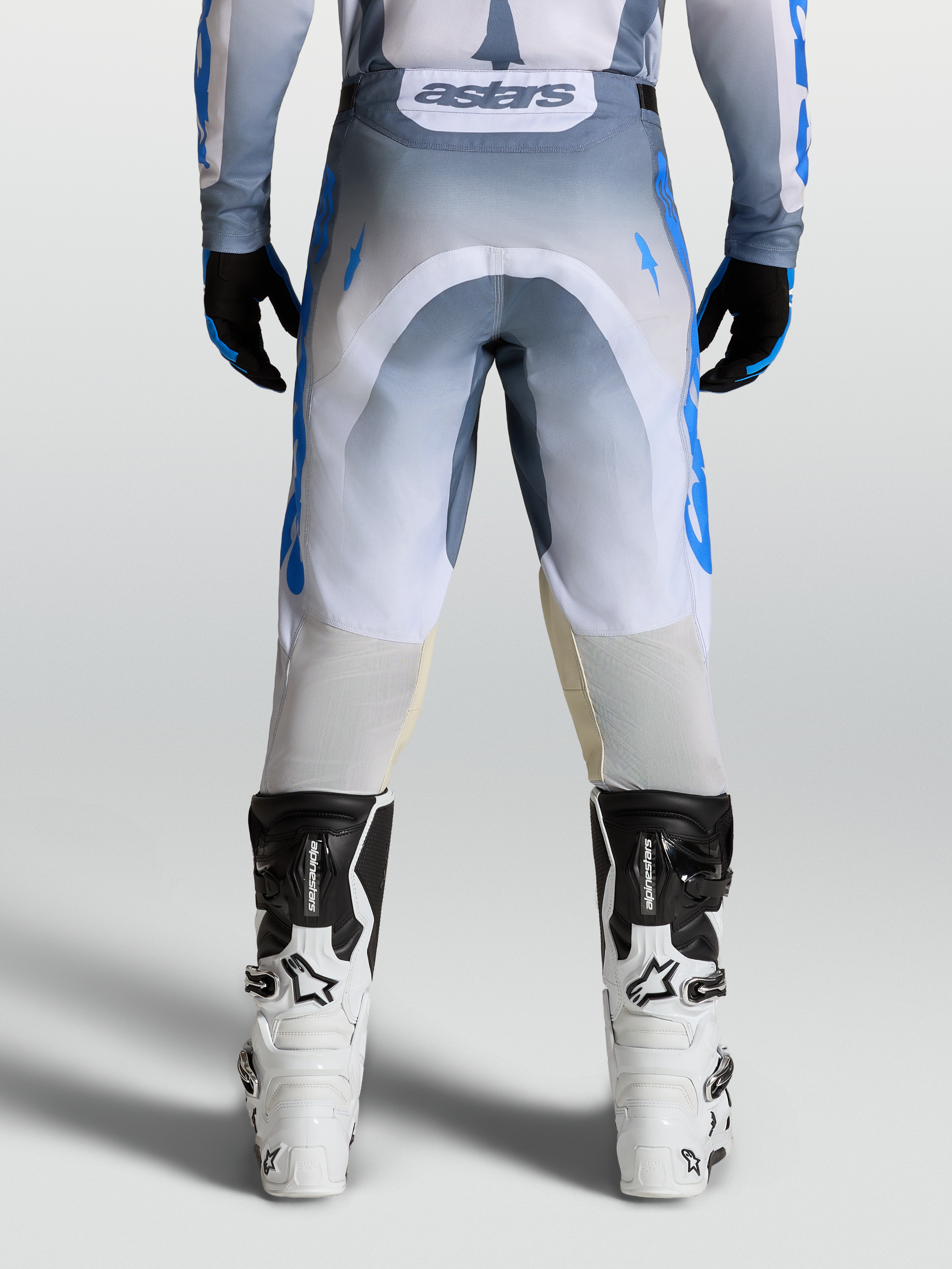 Alpinestars Racer Amber Broek voor heren, motocrossbroek in grijs en blauw, achterzijde op model met Alpinestars-laarzen, duurzaam 600D polyweefsel.