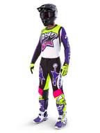Motocross-Fahrer in Alpinestars Limited Edition Supertech Dirt Studios® Ausrüstung, Farbkombination in Weiß, Lila und Neongelb, schwarze Hose mit auffälligen lila und pinkfarbenen Stern-Logos, neongelbe Handschuhe, lila-weiße Rennstiefel, schwarzer Helm, komplette professionelle Rennausrüstung für Offroad-Performance