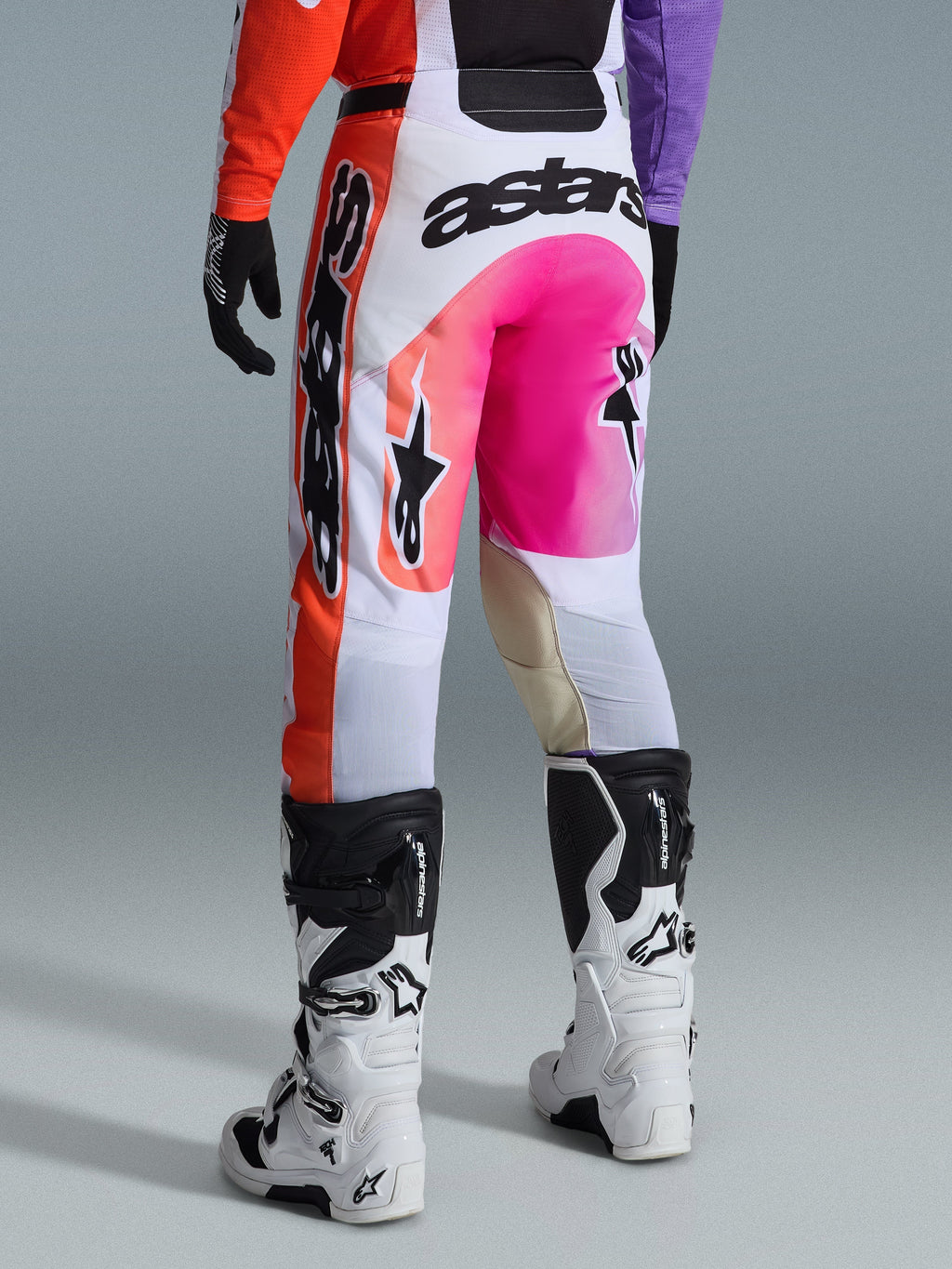 Pantalon Alpinestars 2026 Racer Air Portl, pantalon de motocross, multicolore avec blanc, rose vif et orange, vue arrière porté avec des bottes Alpinestars blanches et noires, logo audacieux et construction de course durable