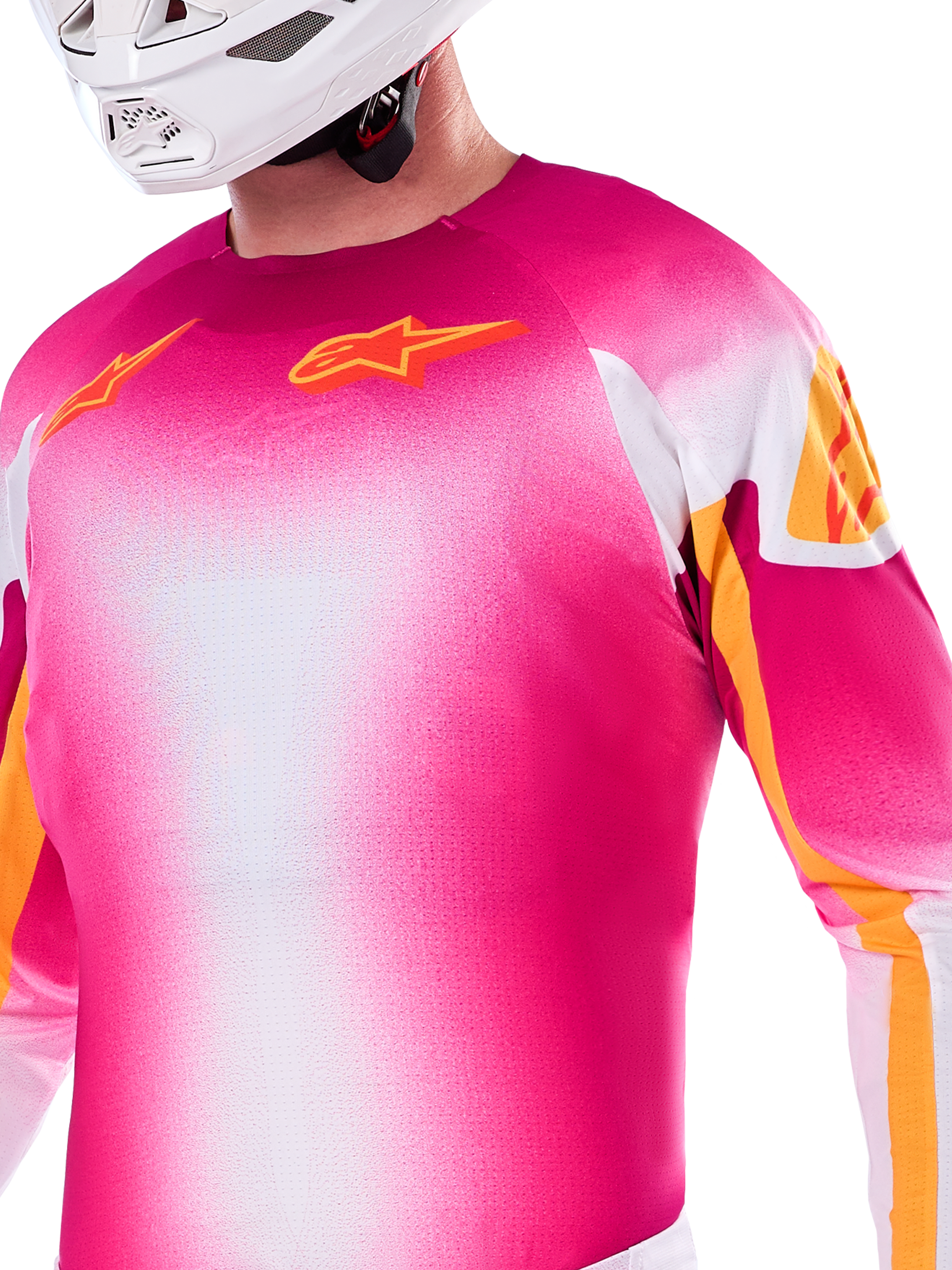 Alpinestars Limited Edition Supertech AFD MIG Jersey, Motocross-Jersey mit Farbverlauf in Pink Fluo und Weiß, mit orangefarbenen Astars-Logos und Ärmelakzenten, getragen von einem Fahrer mit weißem Helm, athletische Racing-Passform.