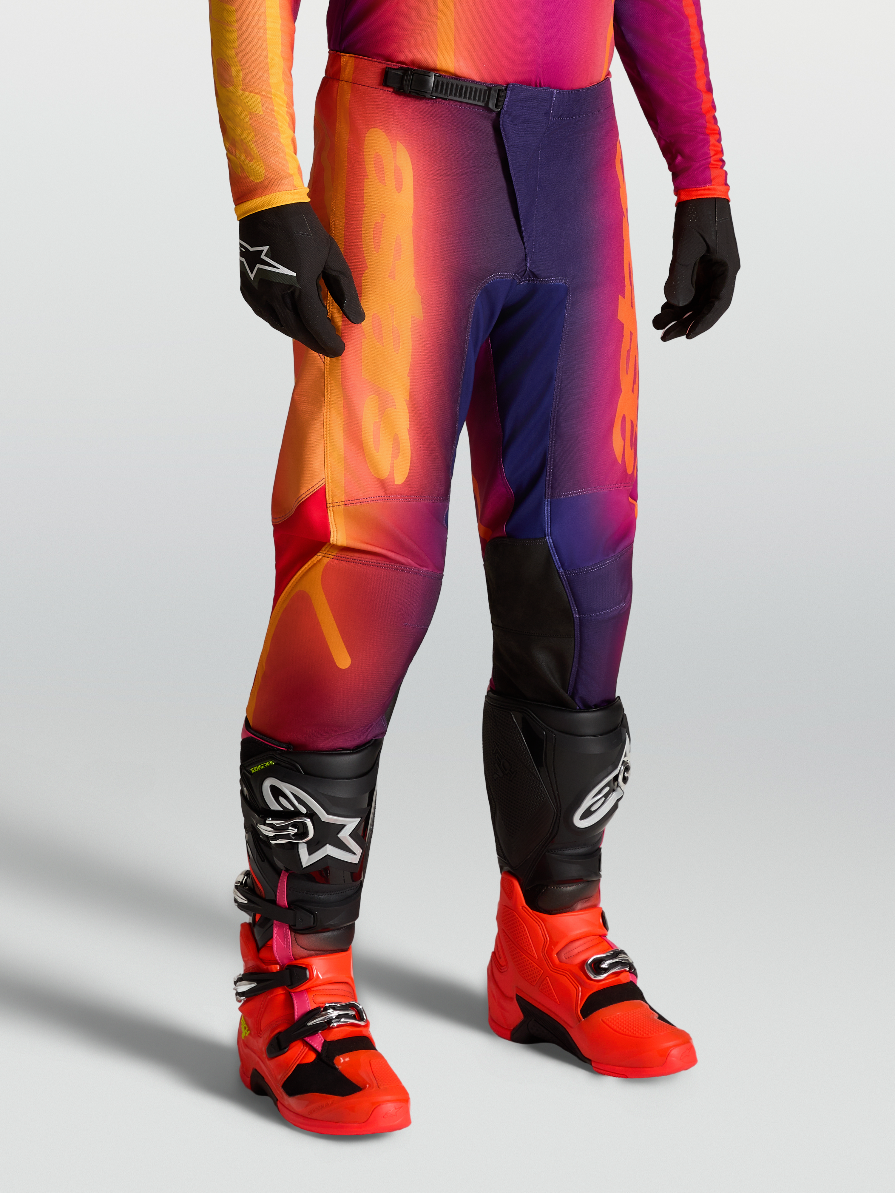 Alpinestars Fluid Kepler Pants for motocross, sport-fit off-road pants in purple and orange, featuring reinforced knees and ergonomic pre-curved design, worn with Tech series boots.