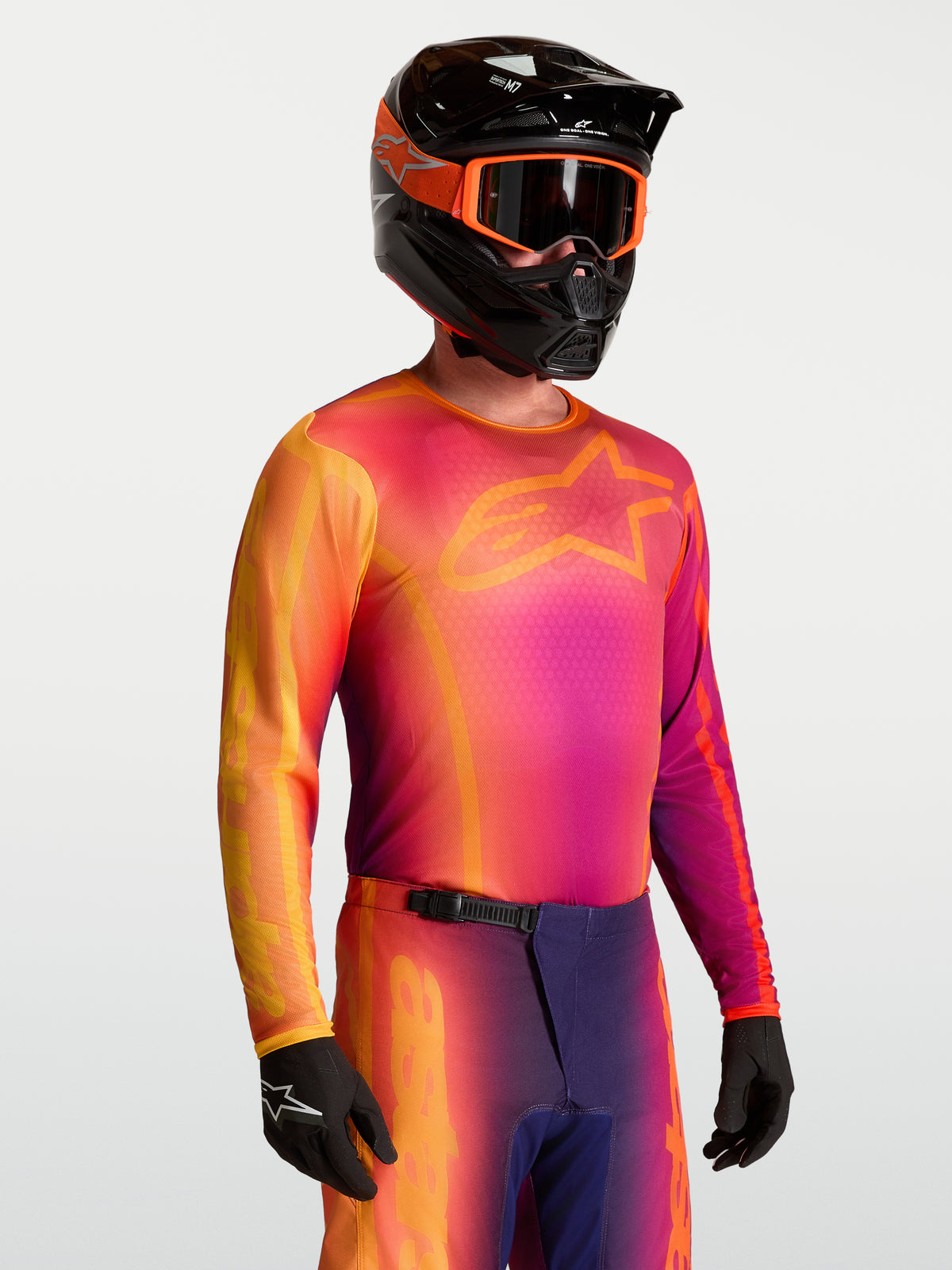 Alpinestars Fluid Kepler Trikot, Herren-Motocross-Trikot, Lila und Orange, feuchtigkeitsableitende Polygewebekonstruktion, getragen von einem Model mit Helm.