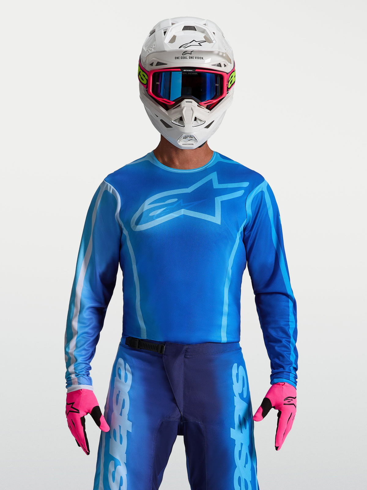 Alpinestars maillot Fluid Kepler, maillot de motocross pour homme, bleu et bleu clair, coupe ergonomique en poly-tissu léger, porté avec casque et gants roses, idéal pour le tout-terrain et l'enduro.