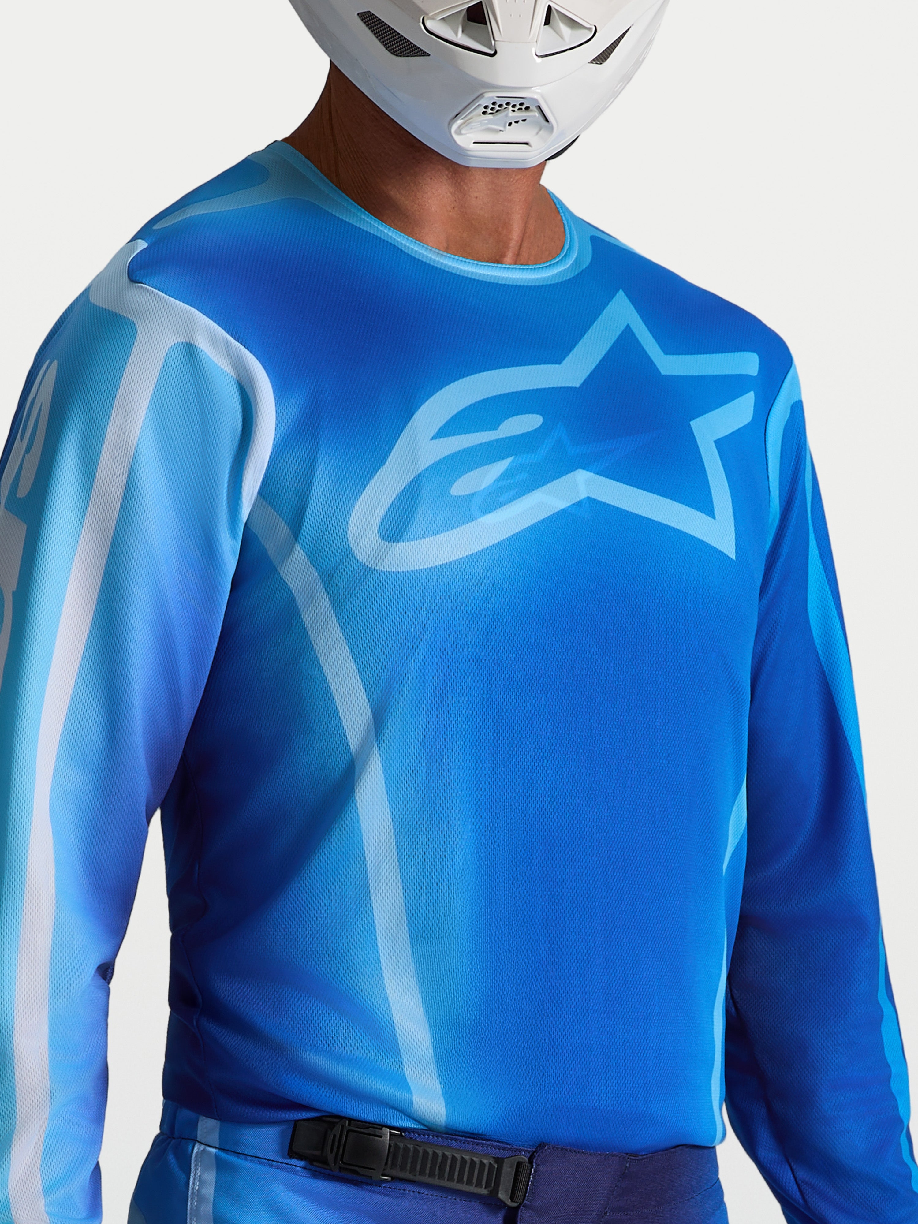Alpinestars Fluid Kepler jersey, blauwe motorcrossjersey voor heren, UCLA blauw en lichtblauw, vochtafvoerend en ademend, sportieve pasvorm, gedragen door een rijder met witte helm.