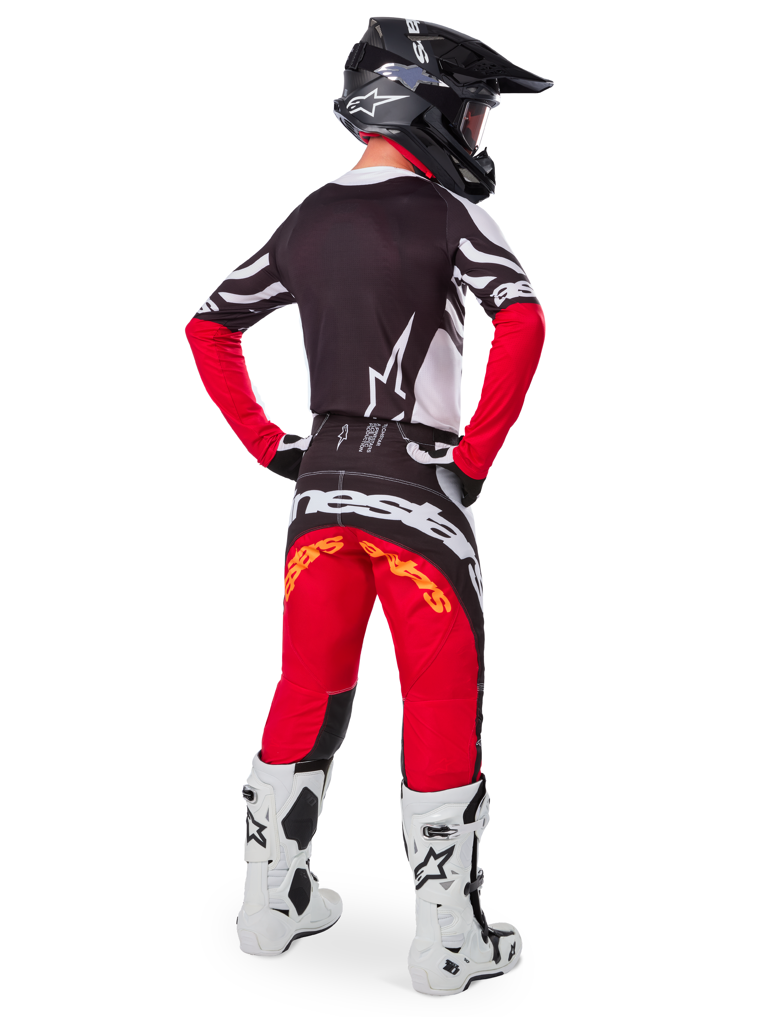 Motocross-Fahrer von hinten im Alpinestars Limited Edition Techstar Deep Trikot in Black White High Red, mit schwarzer Rückseite, weißem Stern-Logo und roten Ärmeln, kombiniert mit einer passenden rot-schwarzen Hose, weiß-schwarzen Stiefeln und einem schwarzen Helm für eine komplette Offroad-Rennausrüstung.