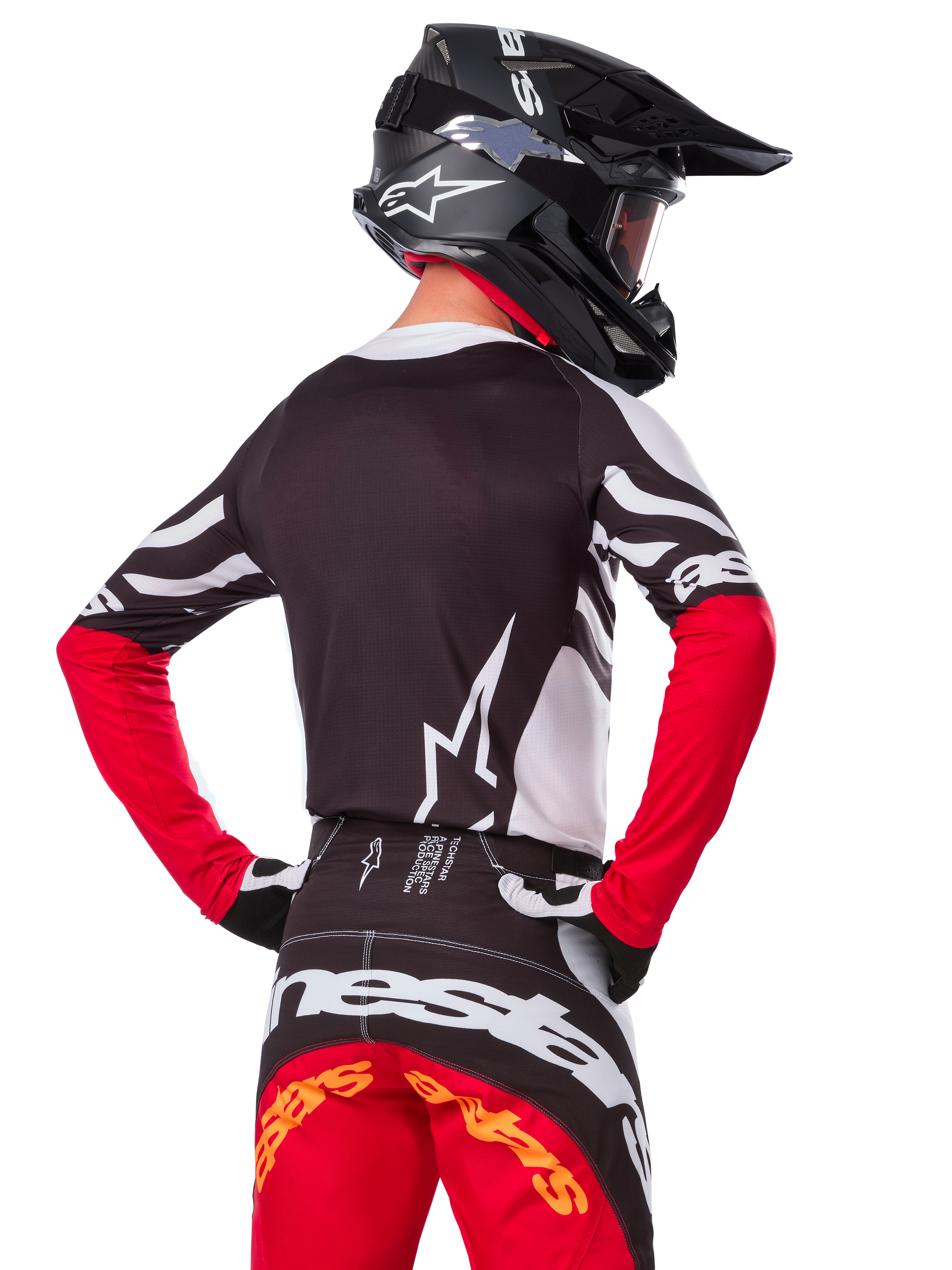 Motocross-Fahrer von hinten mit dem Alpinestars Limited Edition Techstar Deep Jersey in Schwarz, Weiß und High Red, dazu die passende Rennhose und ein schwarzer Helm, athletische Passform für Offroad-Performance