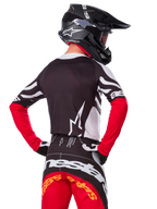 Motocross-Fahrer in kompletter Rennausrüstung, Alpinestars Limited Edition Techstar Deep Jersey in Schwarz, Weiß und High Red, Rückansicht, passende Techstar Deep Hose, schwarzer Helm mit Brille, schwarz-weiße Handschuhe, professionelles Offroad-Rennoutfit