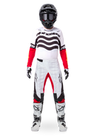Motocross-Fahrer in der Alpinestars Limited Edition Techstar Deep Ausrüstung, weißes Jersey mit schwarzen Wellengrafiken und roten Ärmeln, passende weiß-schwarze Hose mit roten Akzenten, schwarzer Helm mit dunkler Brille und weiße Stiefel, professionelles Offroad-Outfit