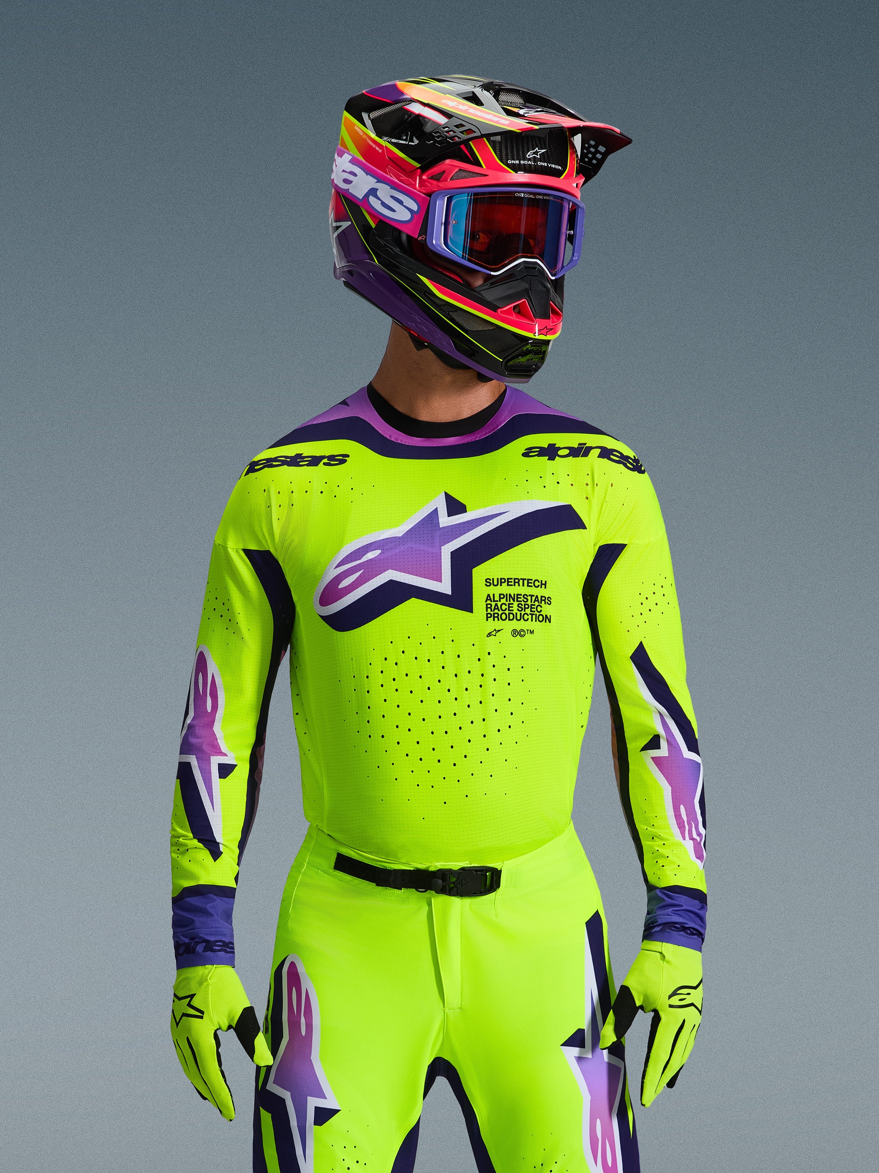 Alpinestars 2026 Supertech Vista Gear Set, motocross rider wearing high-visibility yellow jersey and pants with purple and blue accents, large Alpinestars logo on chest, matching colorful helmet and goggles, pro-level racing outfit
