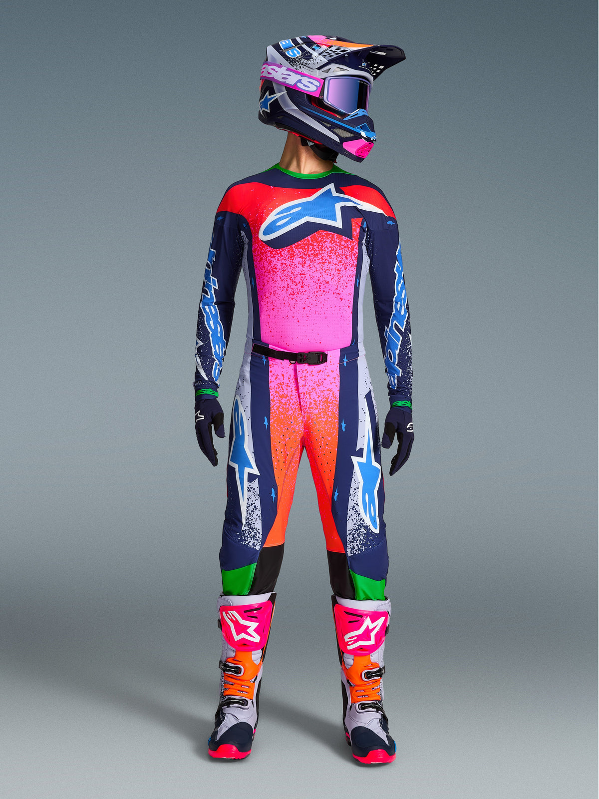 Alpinestars Limited Edition Supertech Records Gear Set, komplette Motocross-Rennausrüstung mit dunkelblauem Trikot und Hose mit leuchtend pinken und orangen Splatter-Mustern, passender Helm, lila Brille und weiße Stiefel mit pinken Akzenten, professionelle Ausrüstung in athletischer Passform für Offroad-Performance