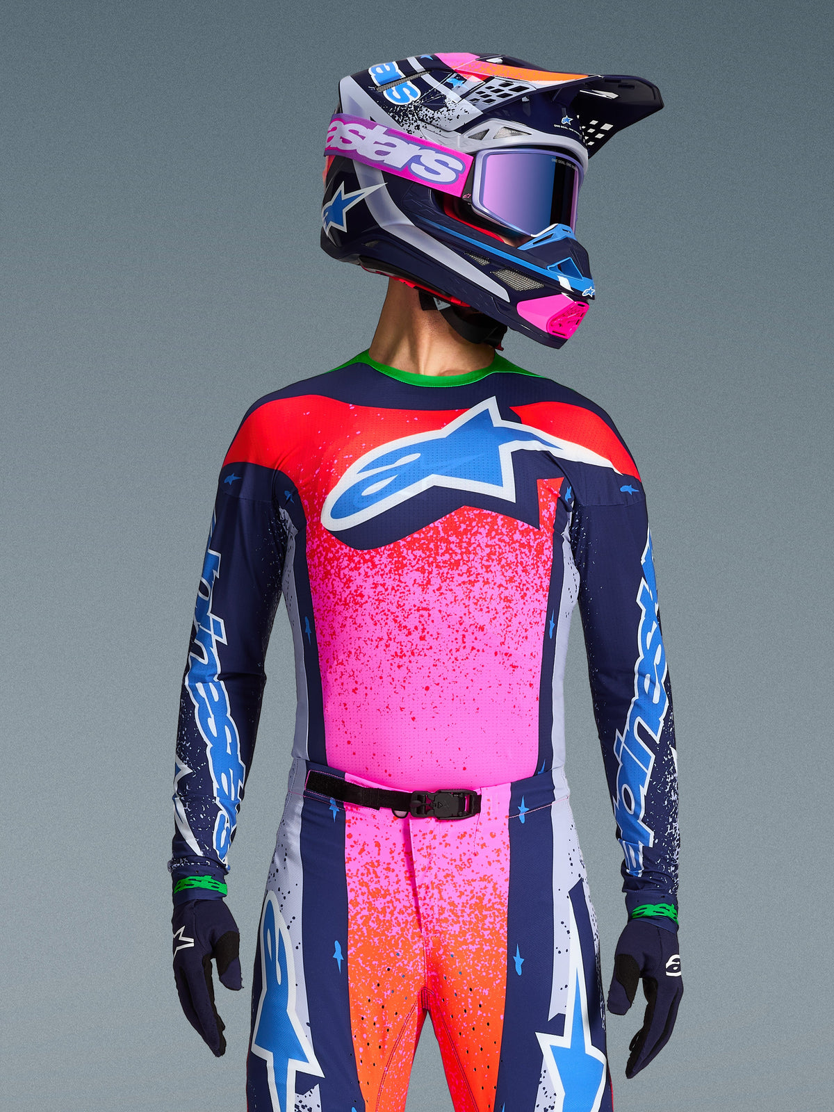 Motocross-Fahrer im Alpinestars Limited Edition Supertech Records Trikot, leuchtendes Design in Pink und Navyblau mit orangefarbenen Sprenkelmustern und einem hellblauen Stern-Logo, passender Helm und Brille, professionelle Rennausrüstung.