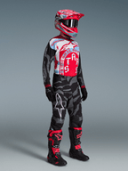 Motorcrossrijder in Techstar Beast Coast kledingset, rood-blauw jersey, camo broek, roze helm en zwarte motorlaarzen.