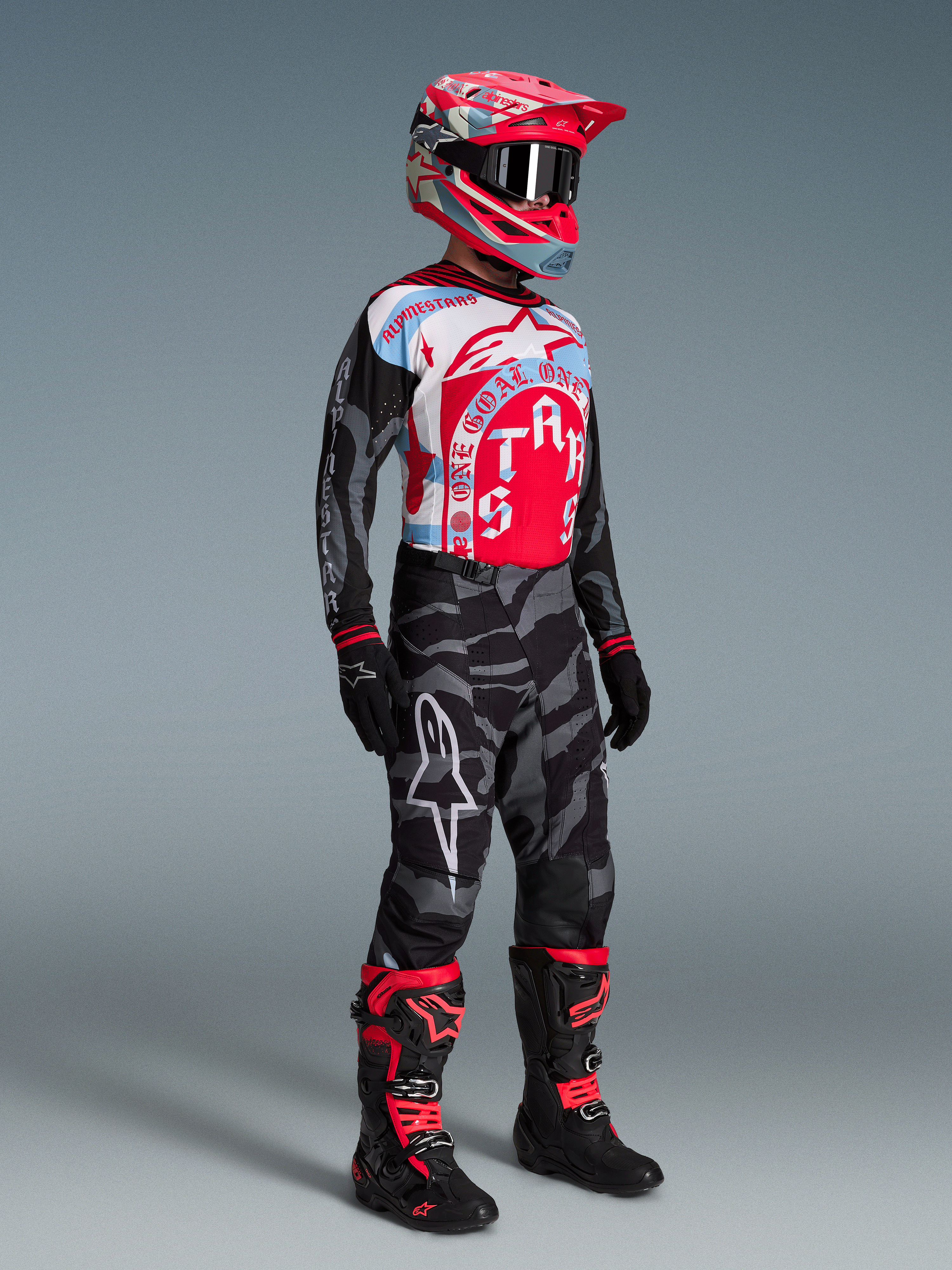 Motorcrossrijder in Techstar Beast Coast kledingset, rood-blauw jersey, camo broek, roze helm en zwarte motorlaarzen.