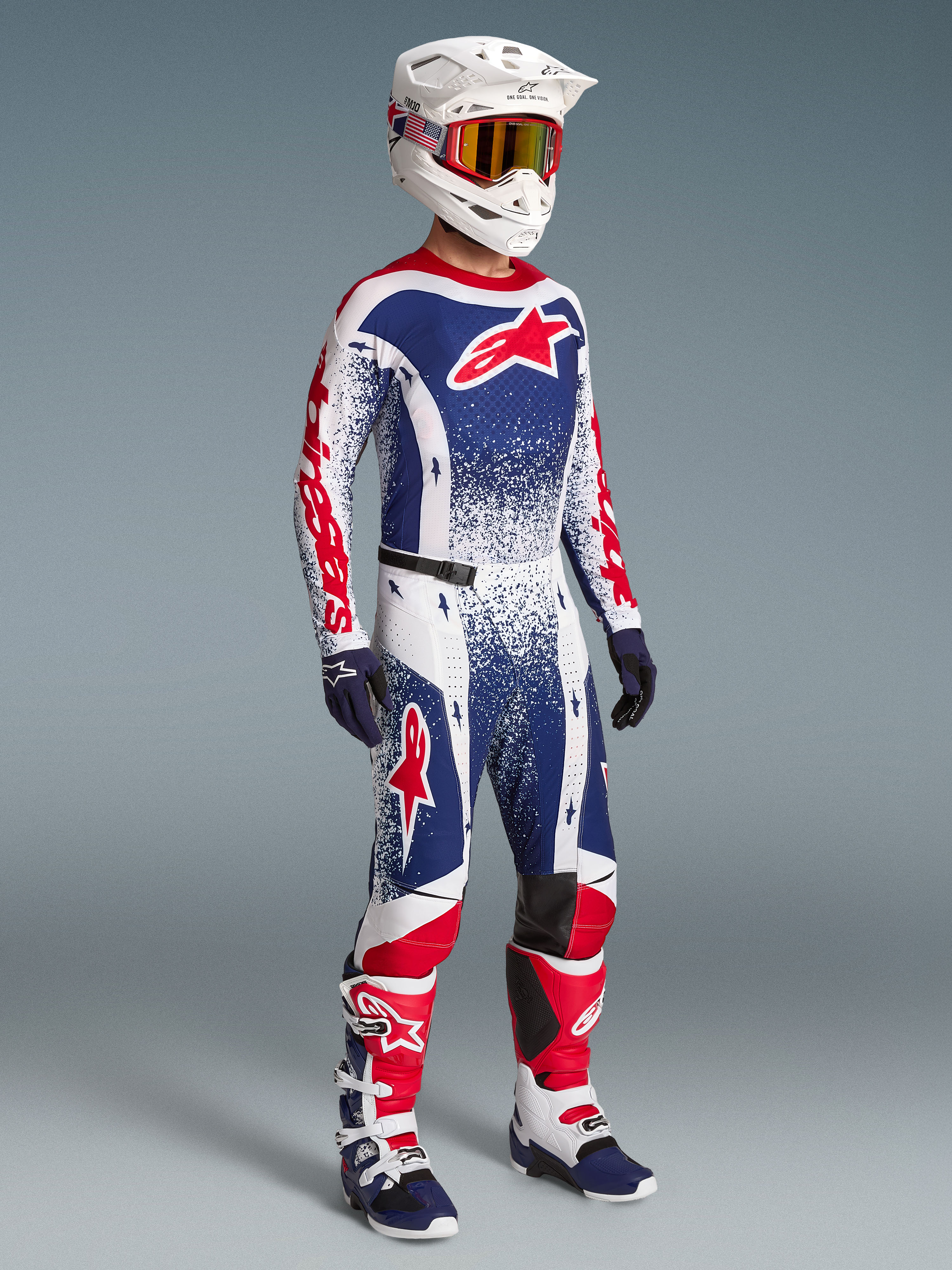 Alpinestars Techstar Unity beperkte oplage kledingset, rood, wit en blauwe motorcrossjersey en broek op model, inclusief bijpassende helm en motorlaarzen.