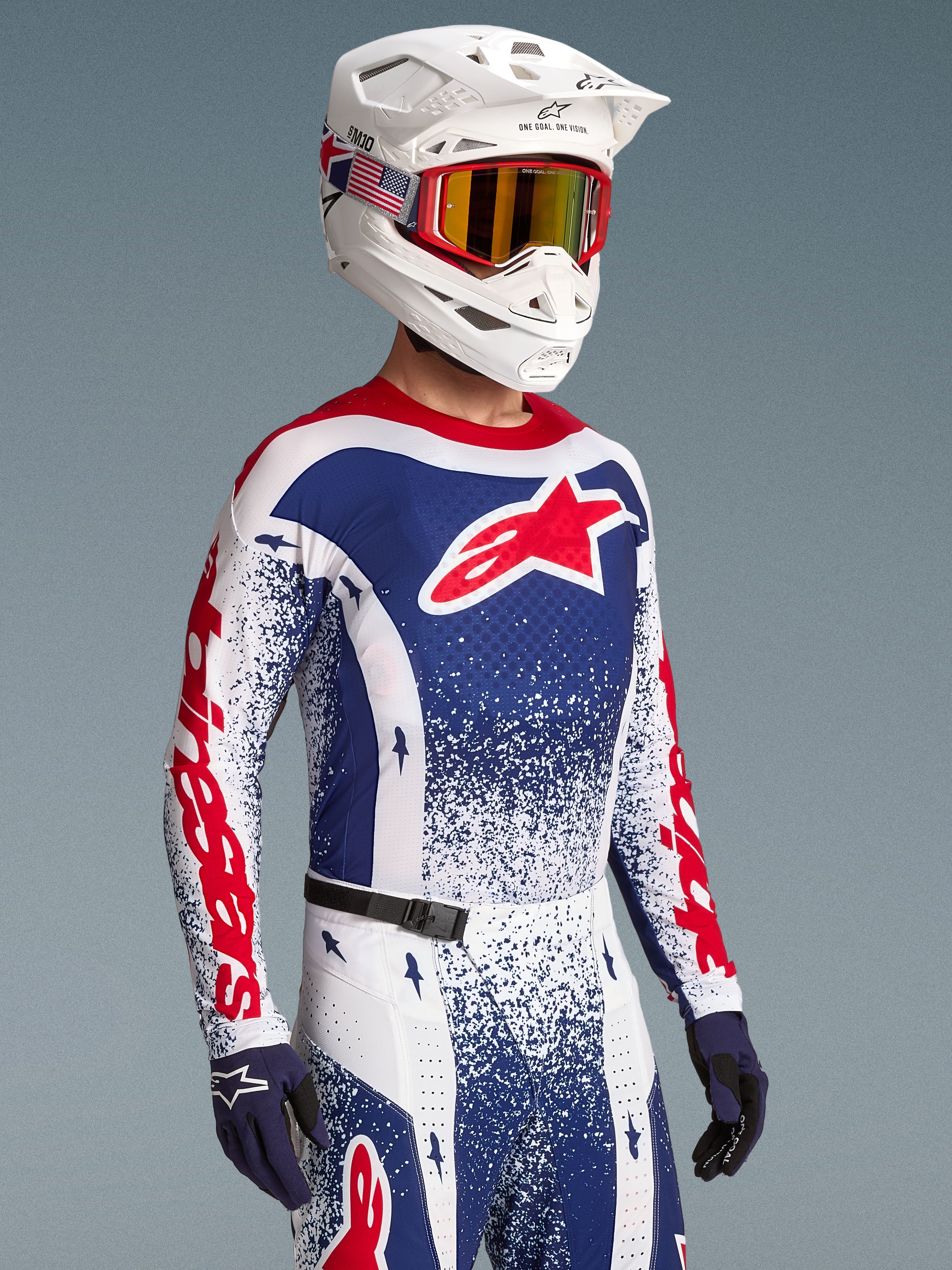 Alpinestars Techstar Unity Beperkte Oplage Kledingset, motorcrossuitrusting voor off-road racing, rood, wit en blauw met stergraphics, gedragen door een model met crosshelm en goggle.