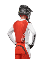 Motocross-Fahrer im 2024 Supertech Ward Jersey in White Hot Orange, Rückansicht mit orangefarbenem Rückenpanel und weißen Ärmeln mit schwarzem Alpinestars-Branding, kombiniert mit passender Hose und einem schwarzen Helm, professionelle Ausrüstung für den Offroad-Rennsport